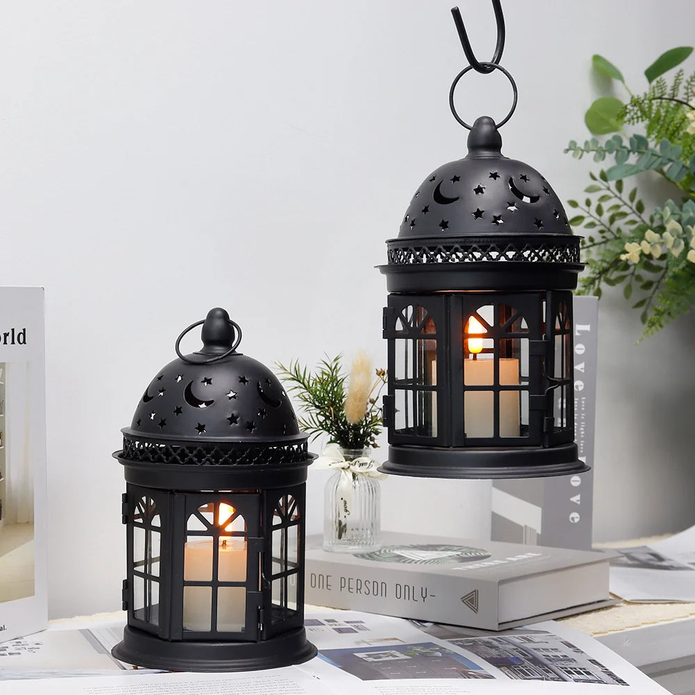 Two black metal lanterns with candles on a surface with books and plants in the background.