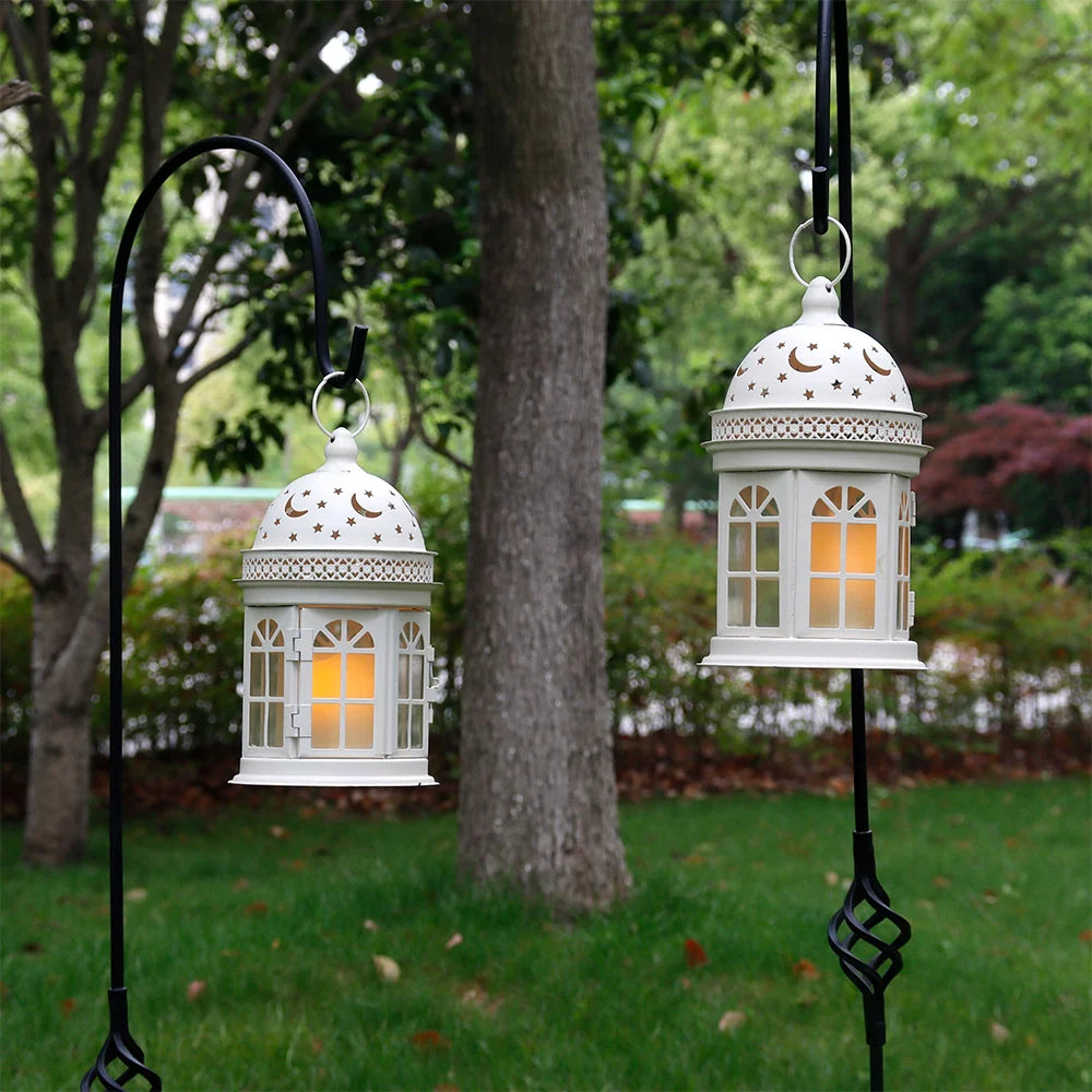 Two white lanterns hanging from stands in a garden setting with trees and grass.