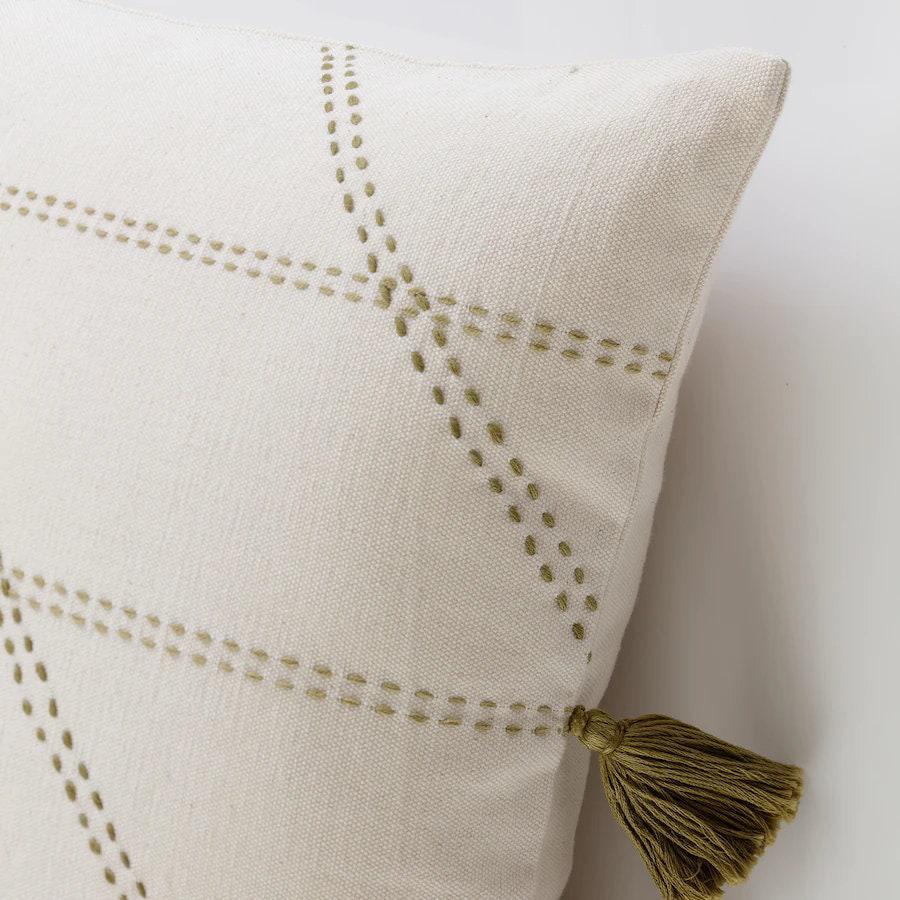 Beige pillow with green stitching and tassel on a white background