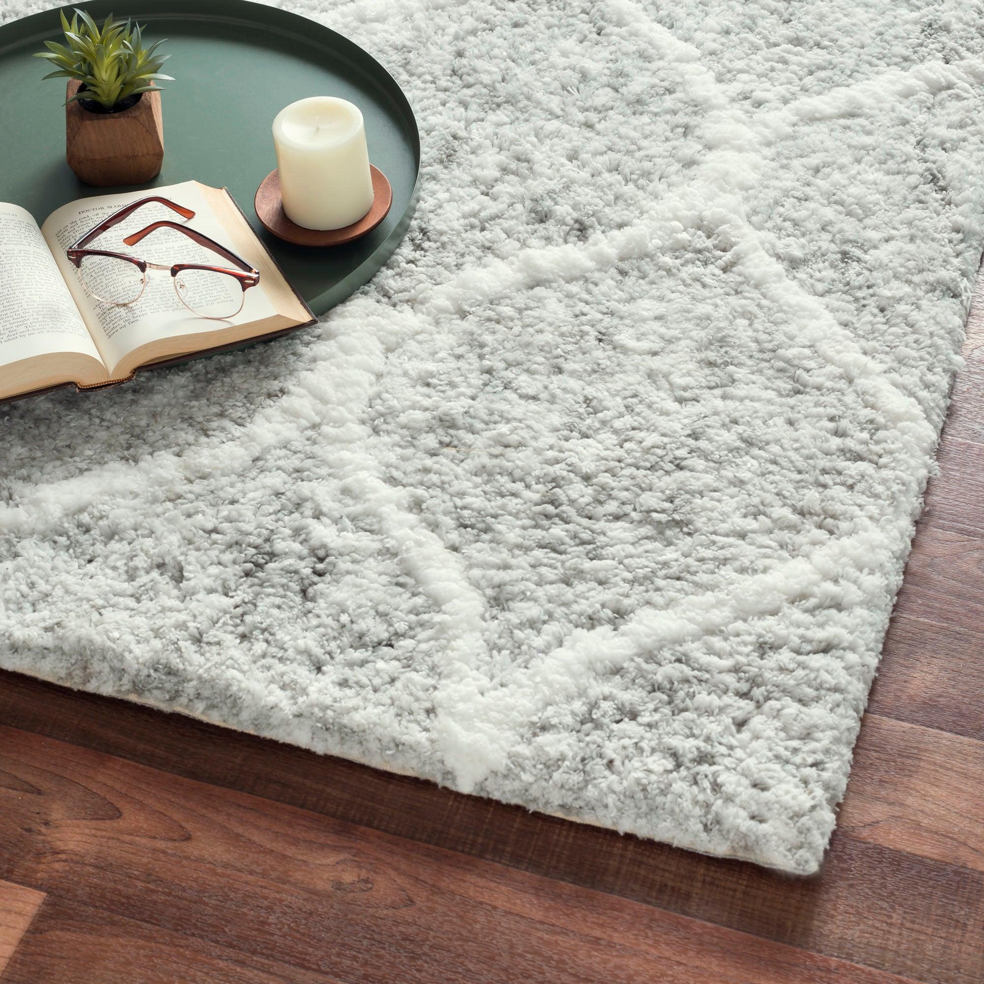 Gray shaggy rug on a wooden floor with a book, glasses, and candle on a green tray.