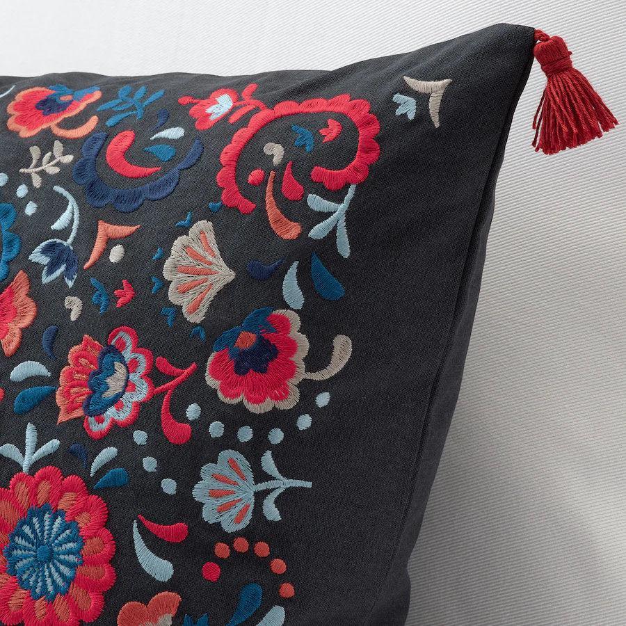 Black pillow with colorful floral embroidery and a red tassel on a light gray background