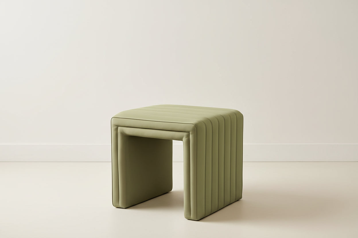 Green ottoman in a room with a wooden cabinet and white vases.