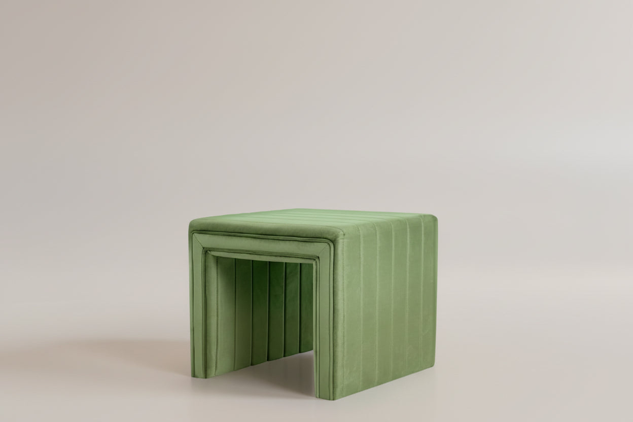 Green cushioned stool in a room with a plant and a chair.
