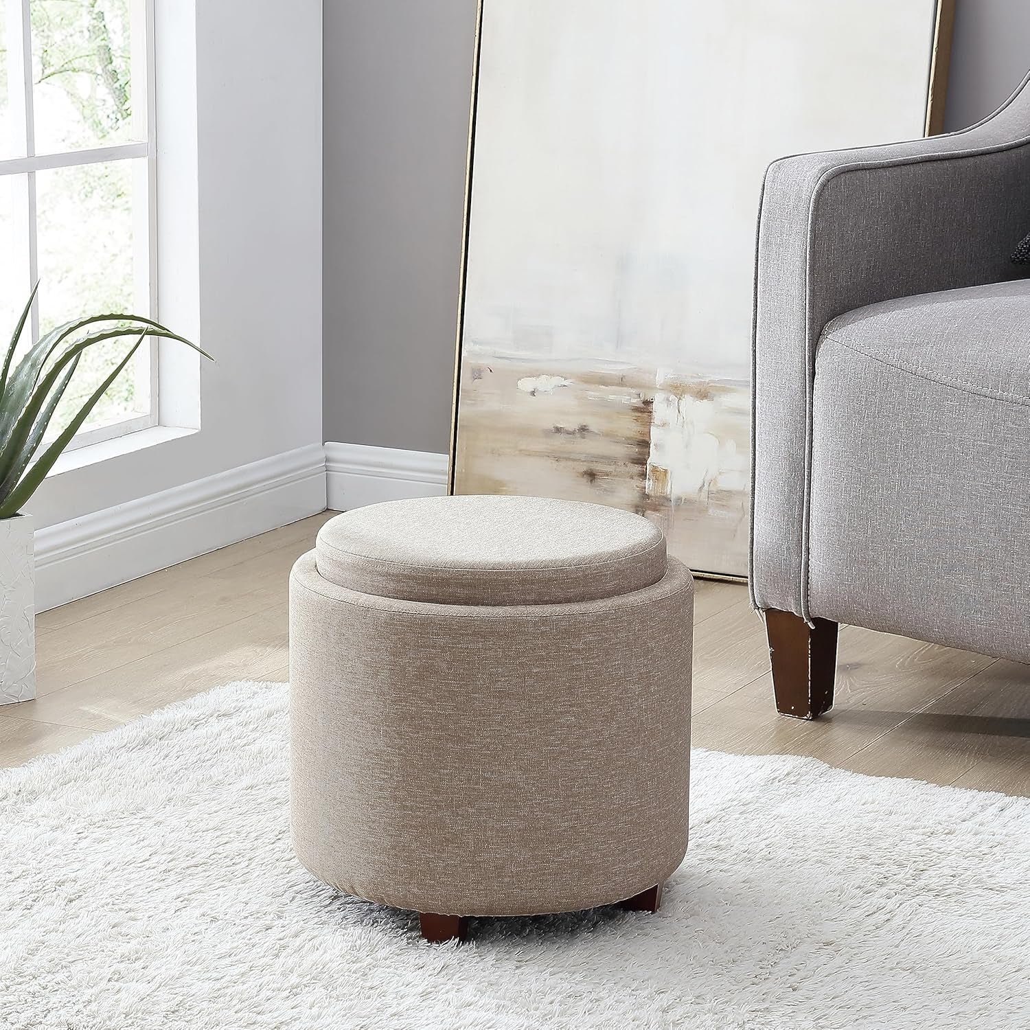 Round beige ottoman with storage compartment in a living room setting.