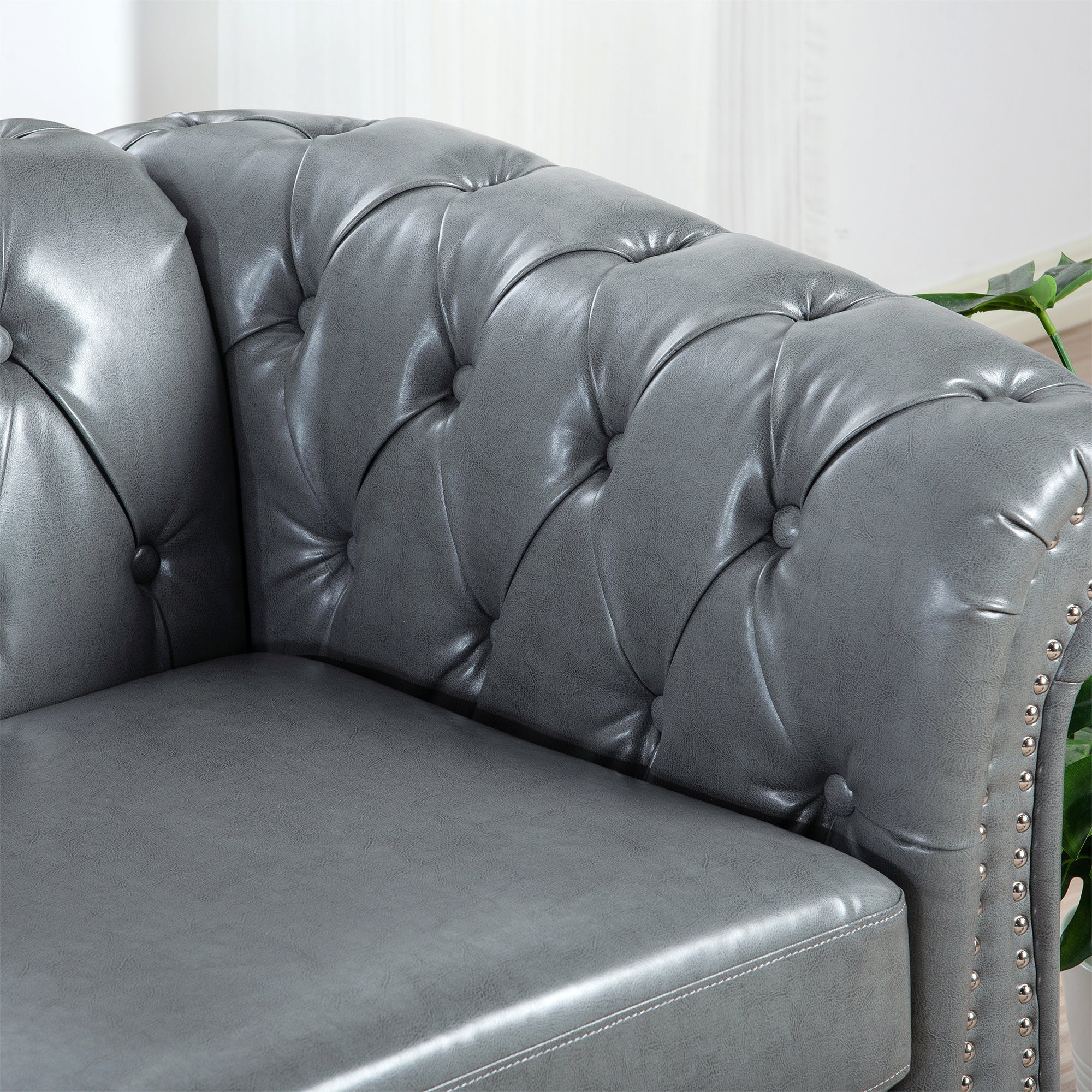 Gray leather sofa with tufted backrest and nailhead trim in a room setting.