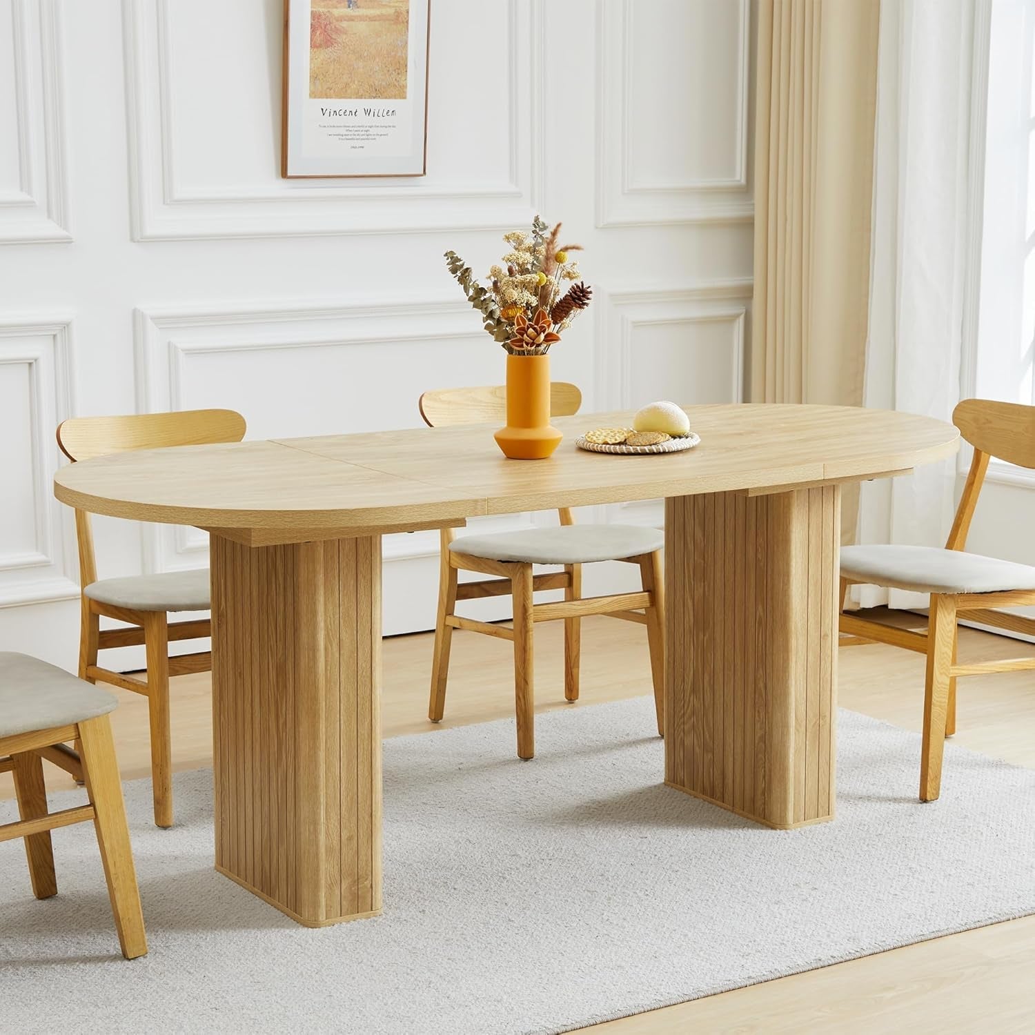 Wooden dining table with chairs in a room with white walls and a painting.