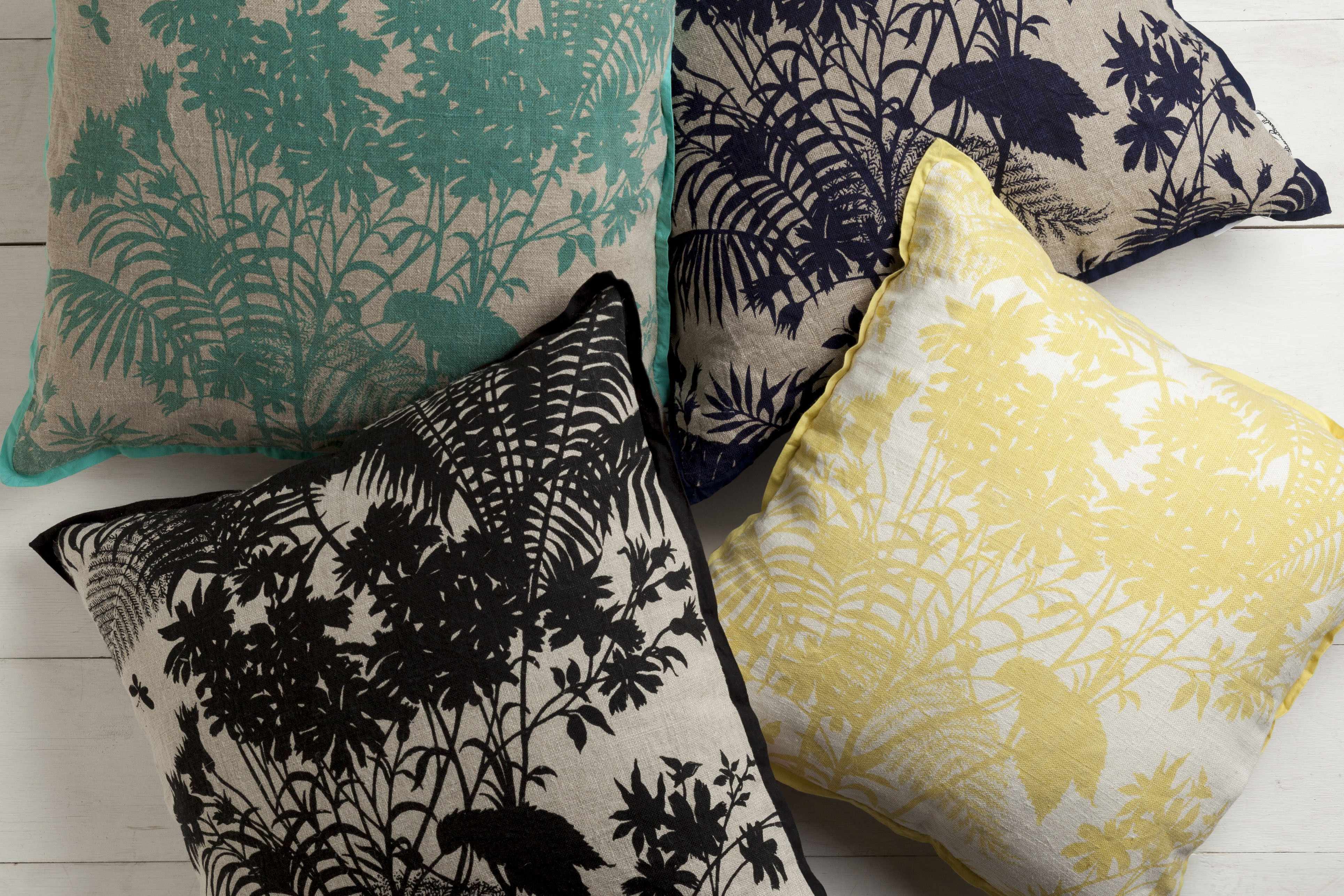 Four decorative pillows with different patterns on a light wooden floor.
