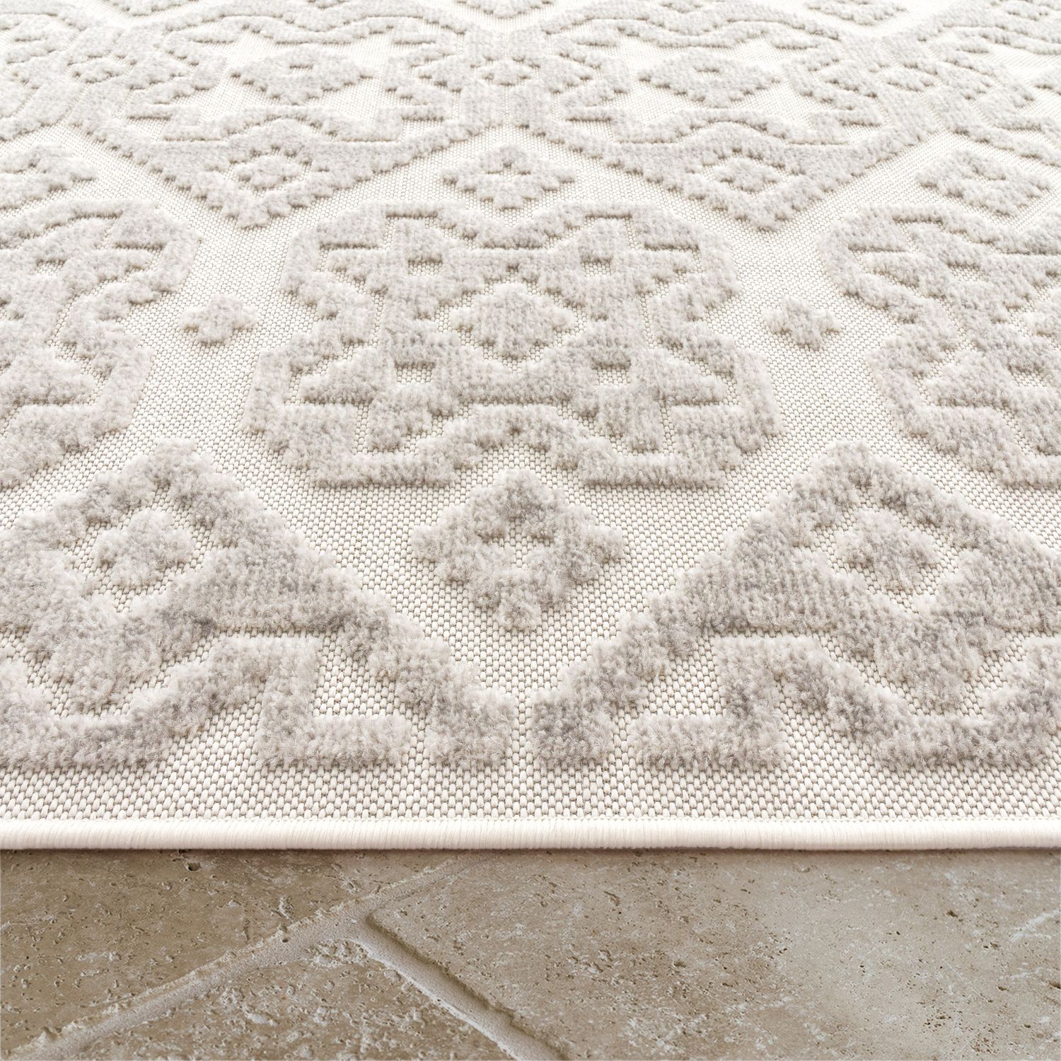 Close-up of a textured beige rug with geometric pattern on a stone floor.