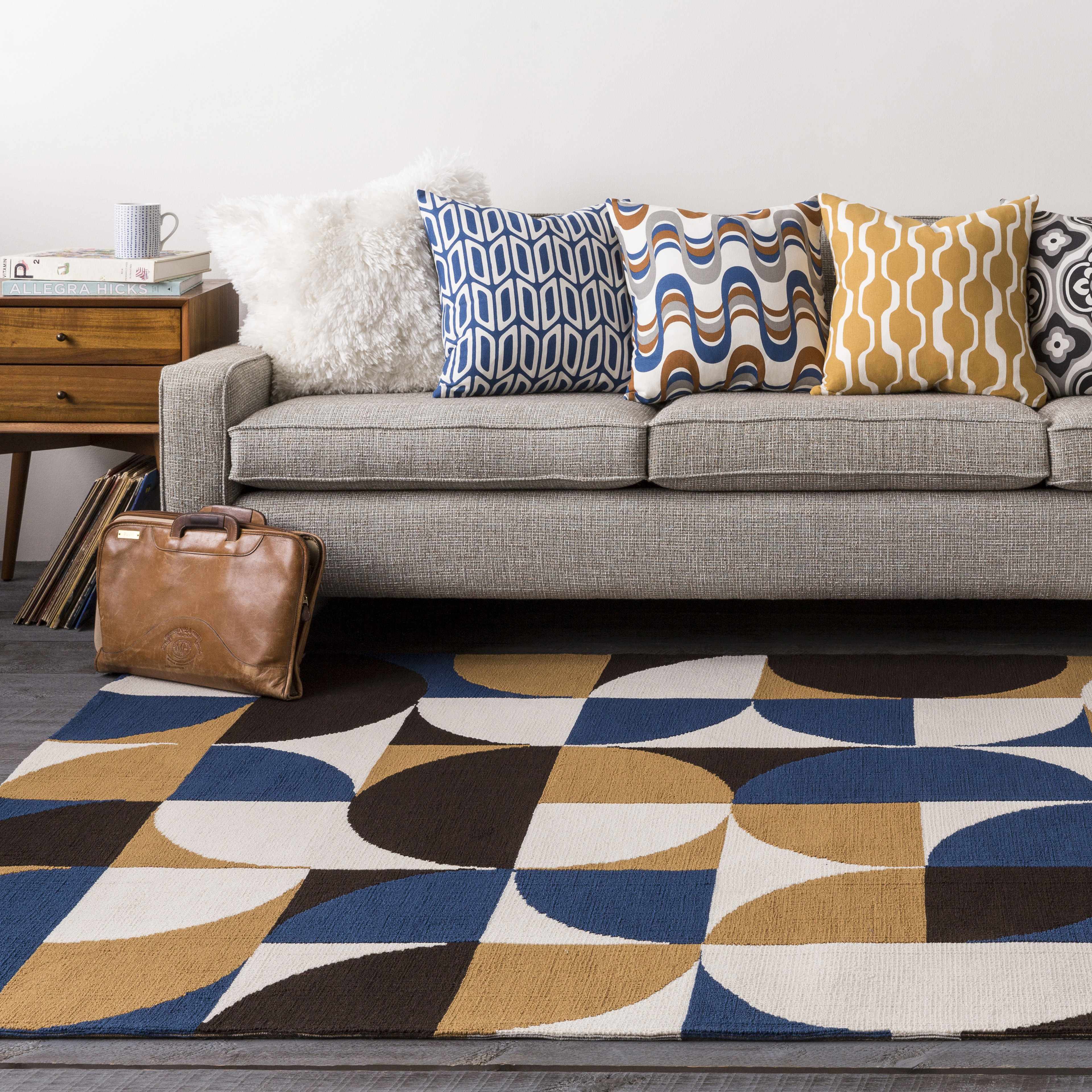Gray sofa with patterned cushions on a geometric rug in a living room setting.