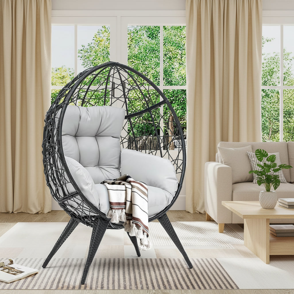 Egg-shaped wicker chair with cushions and a blanket in a room with large windows.