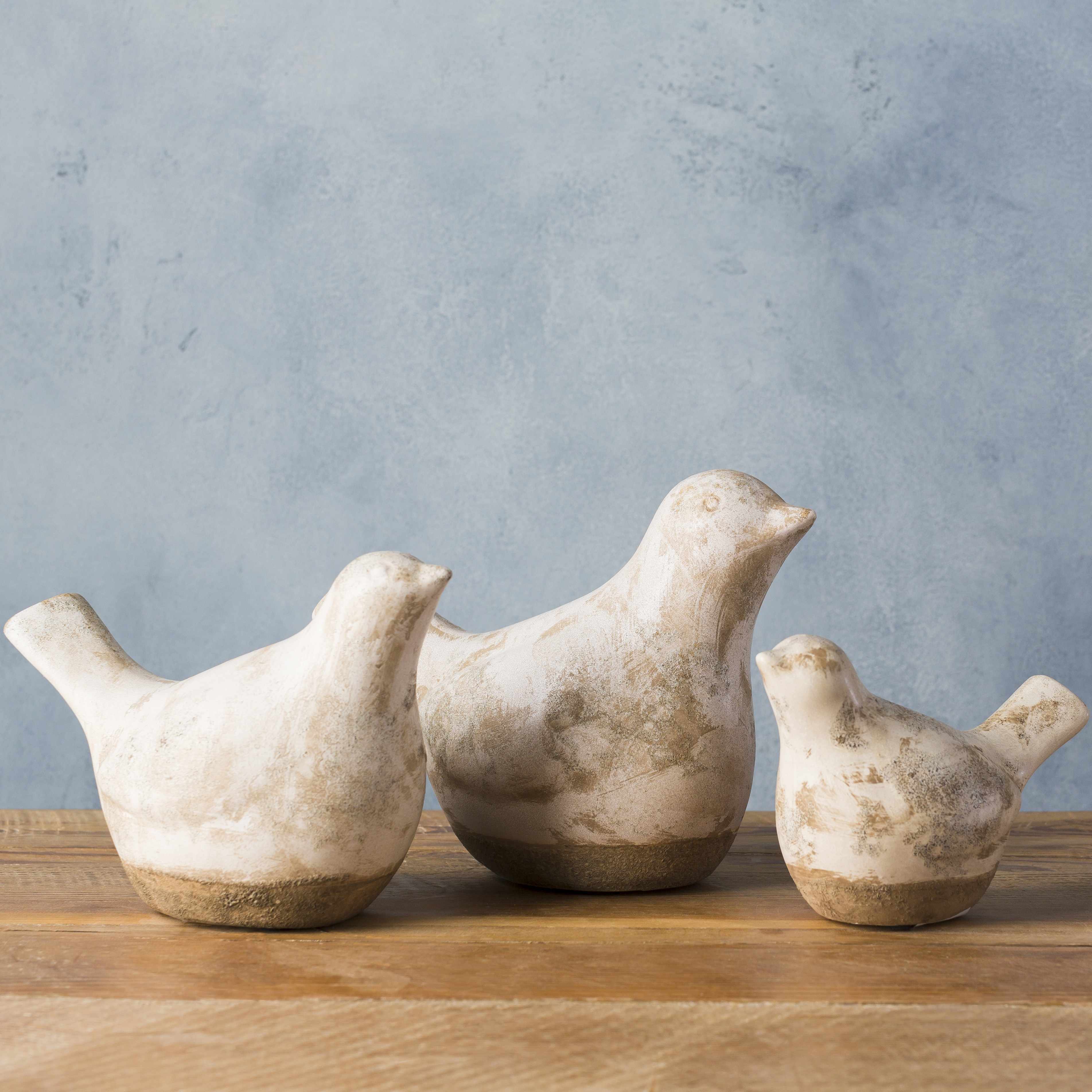 Three ceramic bird sculptures on a wooden surface with a gray background