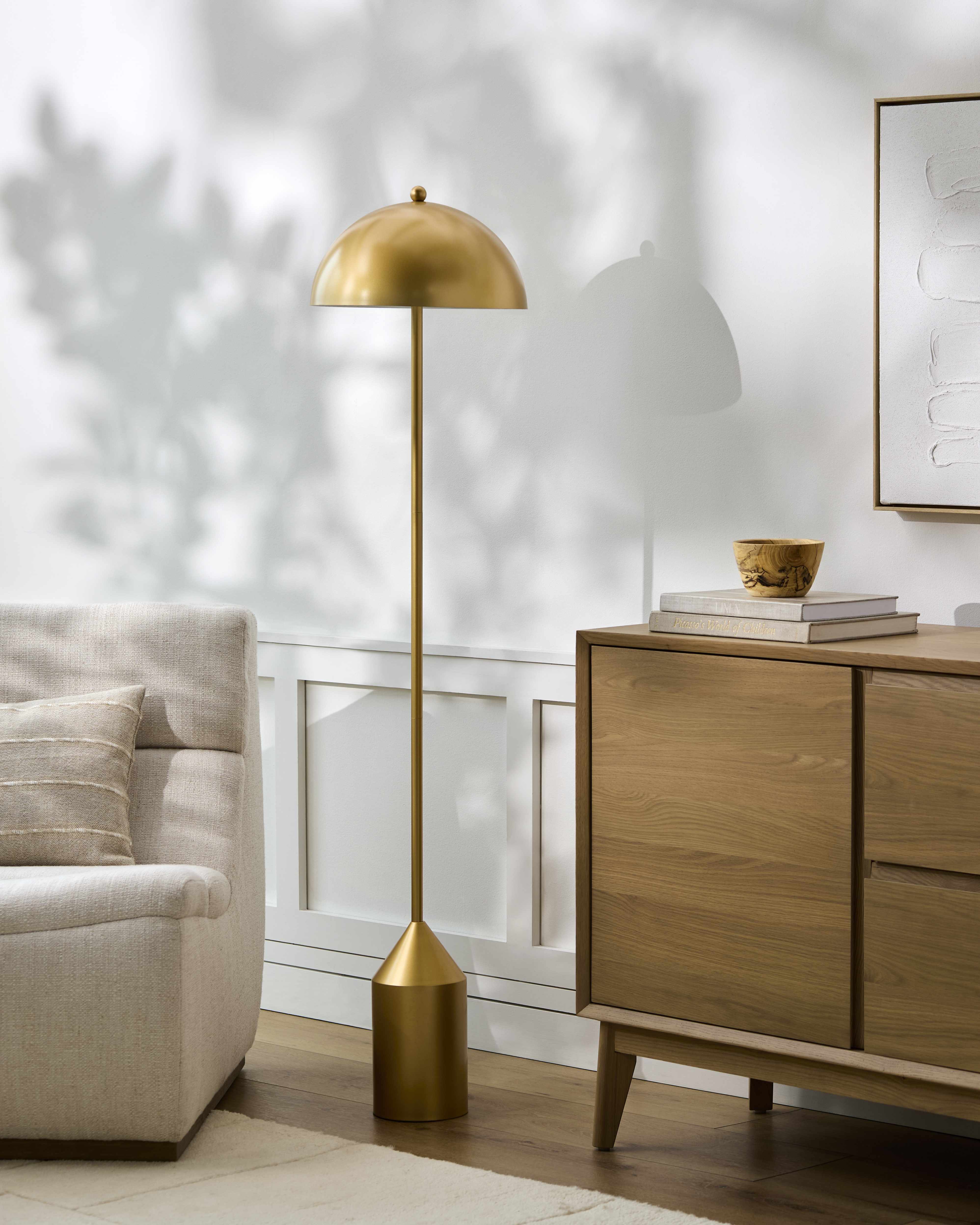Gold floor lamp in a living room setting with a wooden sideboard and sofa.