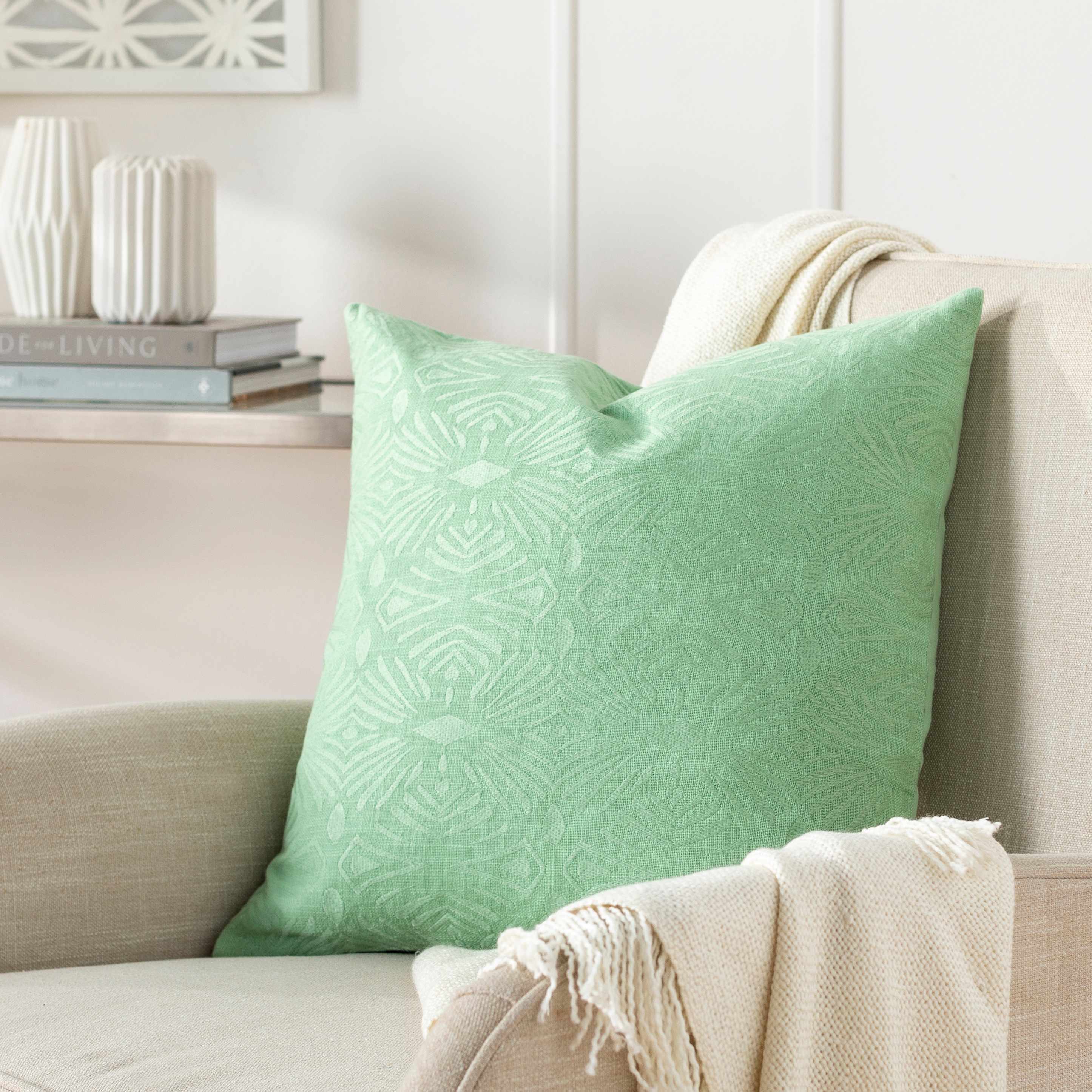 Green patterned pillow on a beige sofa with decorative items in the background