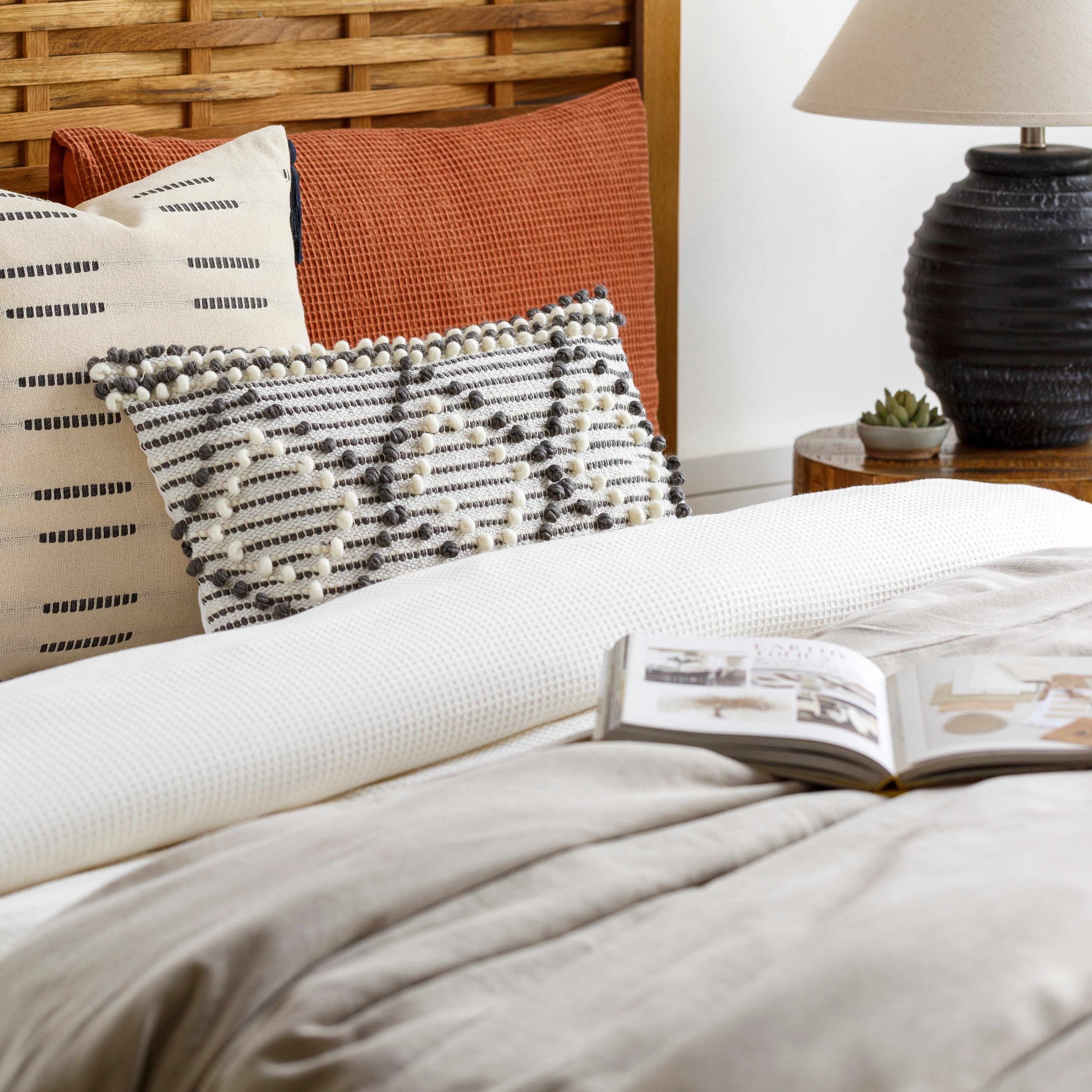 Bed with patterned pillows and an open book, nightstand with lamp in the background