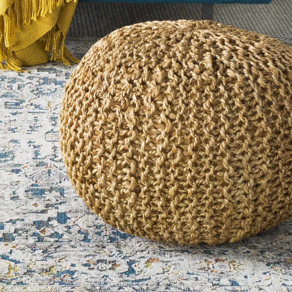 Textured brown pouf on a patterned rug with a yellow blanket in the background