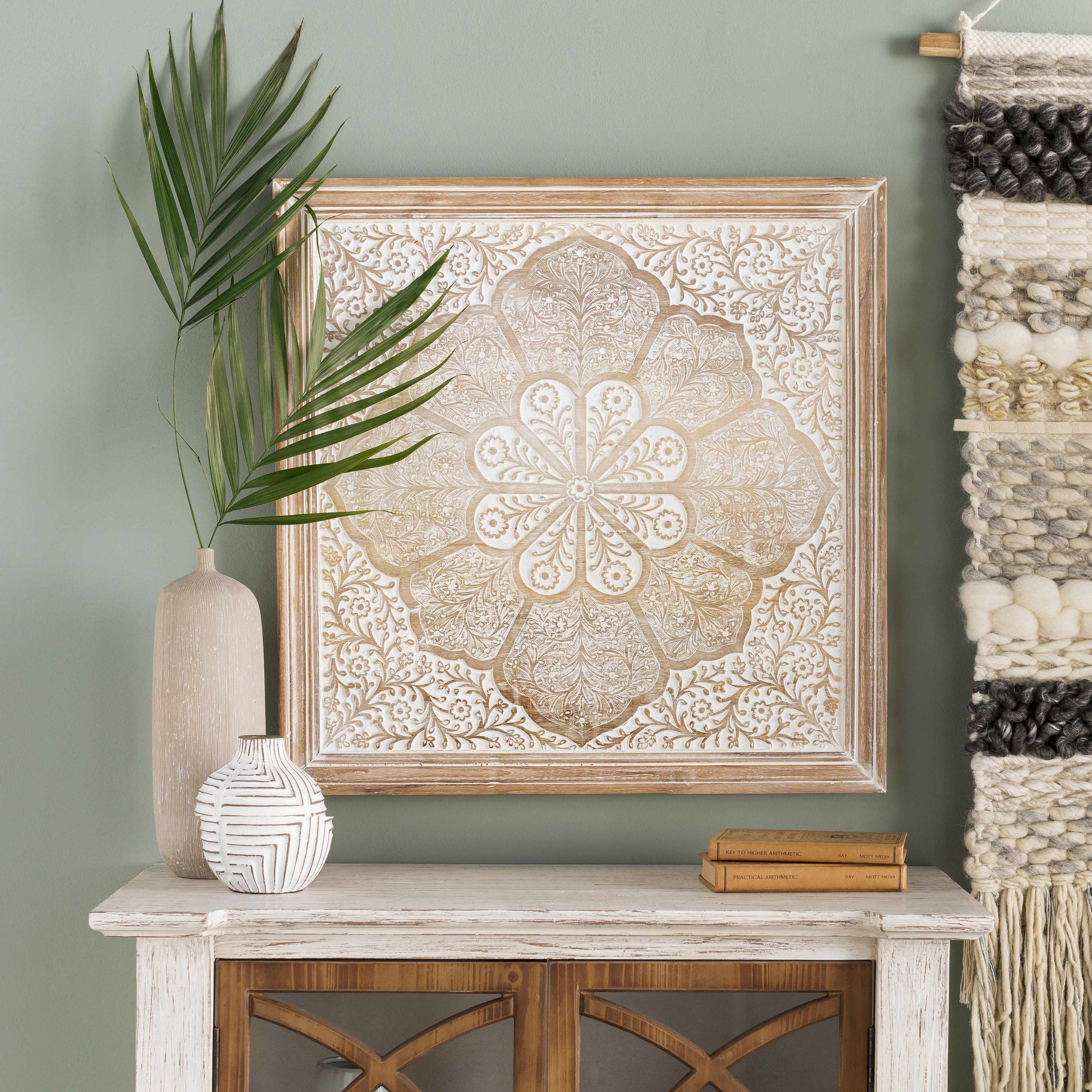 Decorative wall art on a table with vases and a plant against a green wall.
