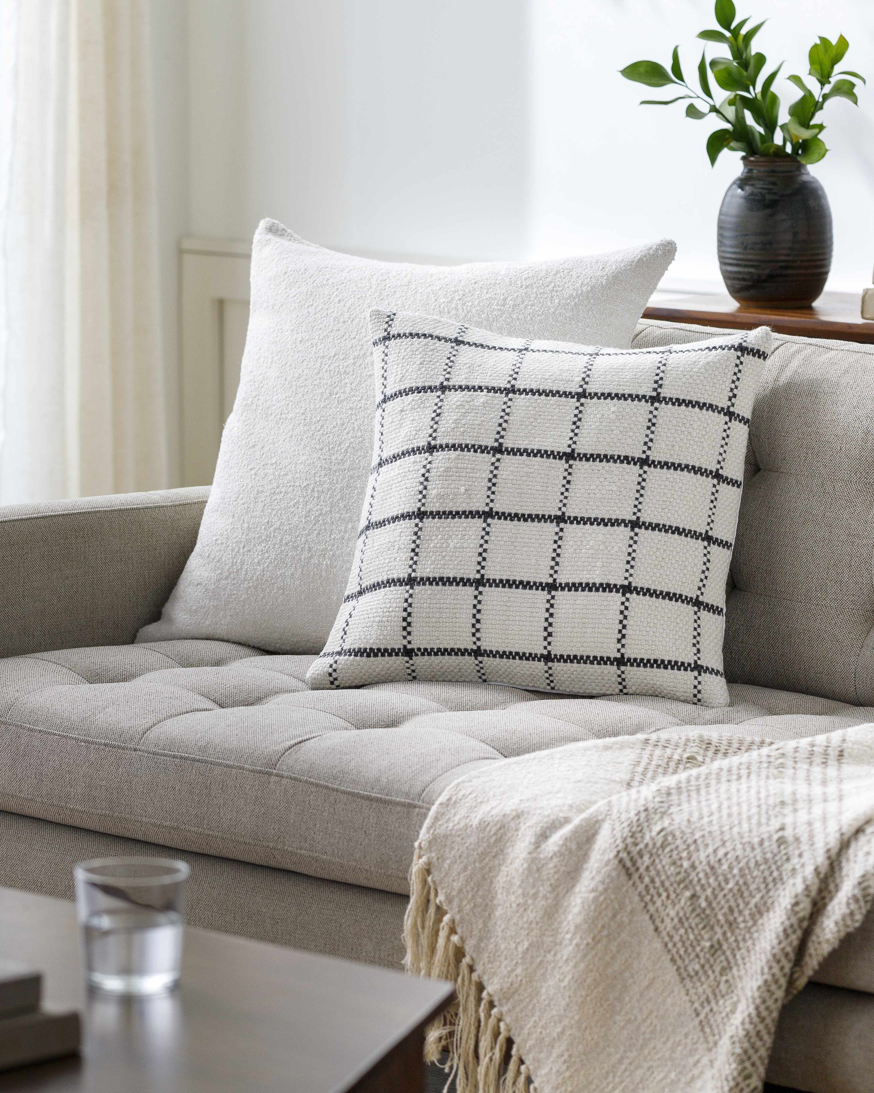 Beige sofa with plaid pillow and blanket in a living room setting