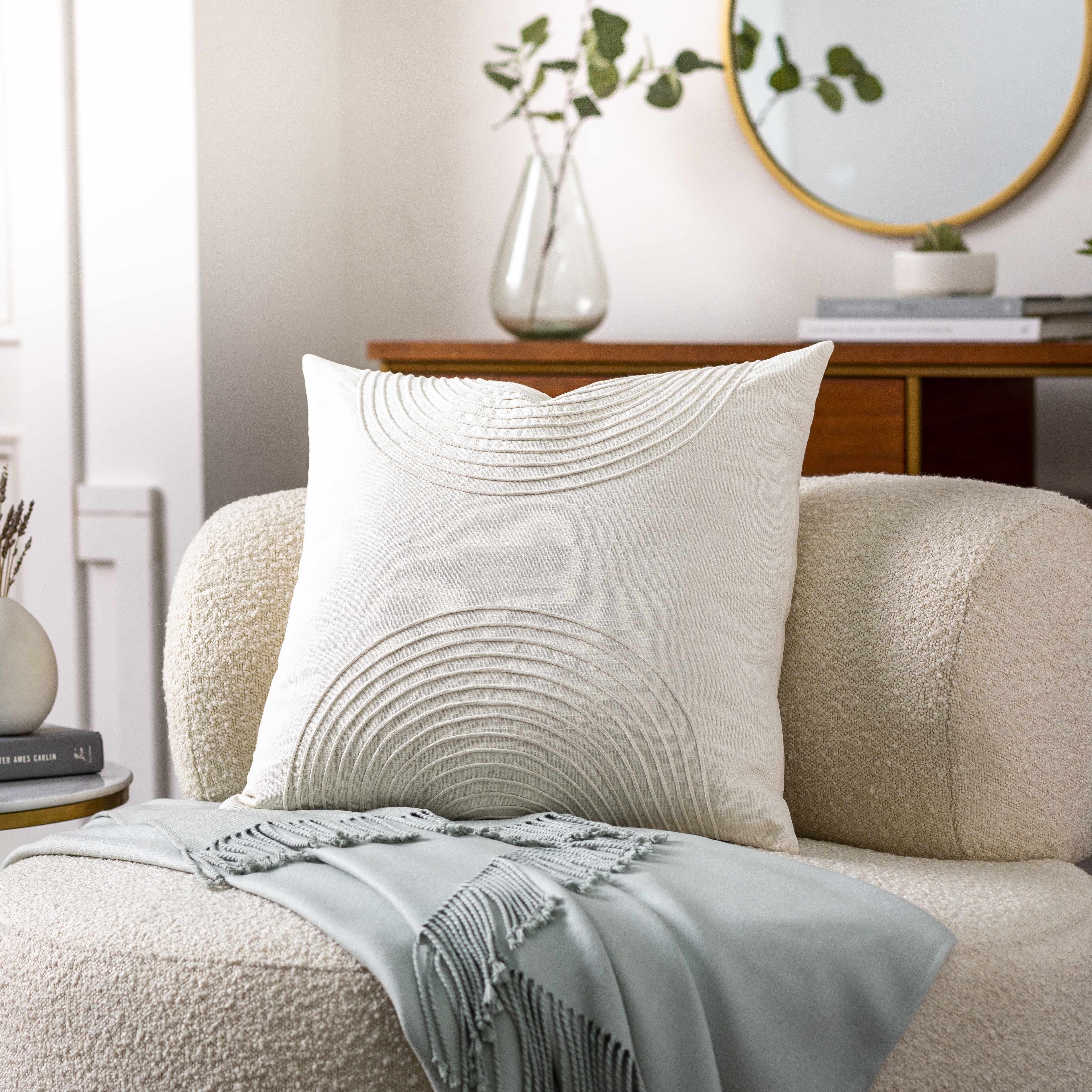 Decorative pillow on a beige sofa with a light blue throw blanket in a home setting.