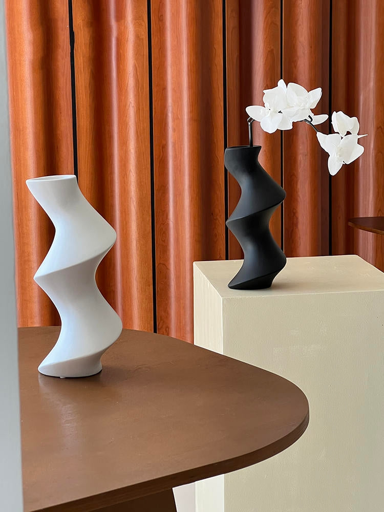 Two abstract vases on a wooden surface with a curtain in the background