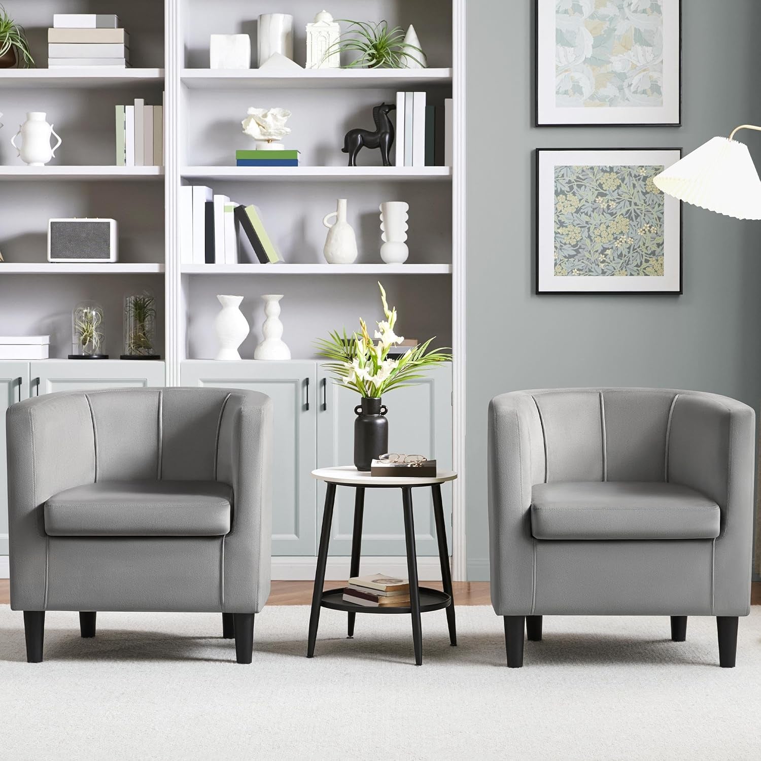 Two gray armchairs in a living room with a side table and shelves.