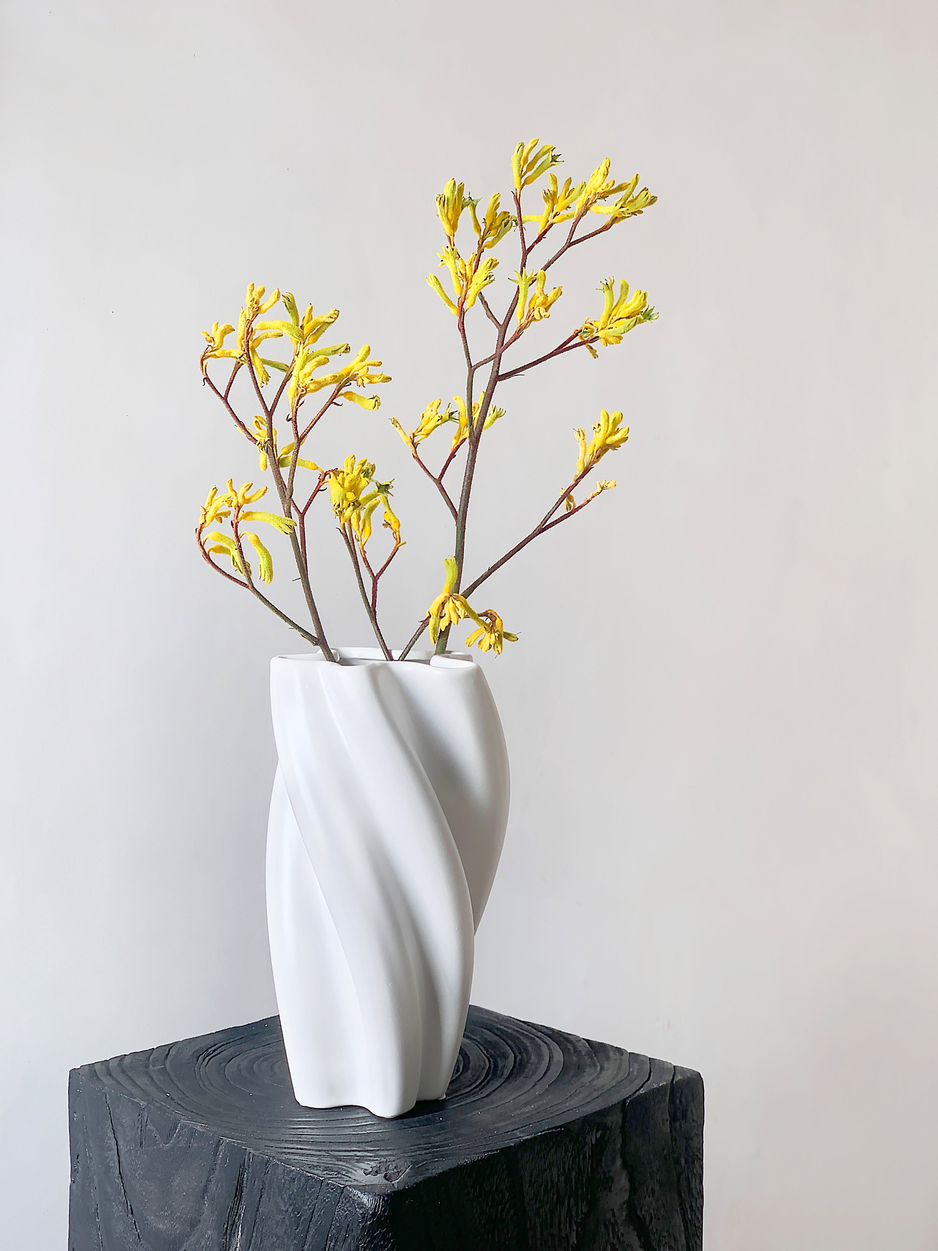 White vase with yellow flowers on a wooden block against a light gray background