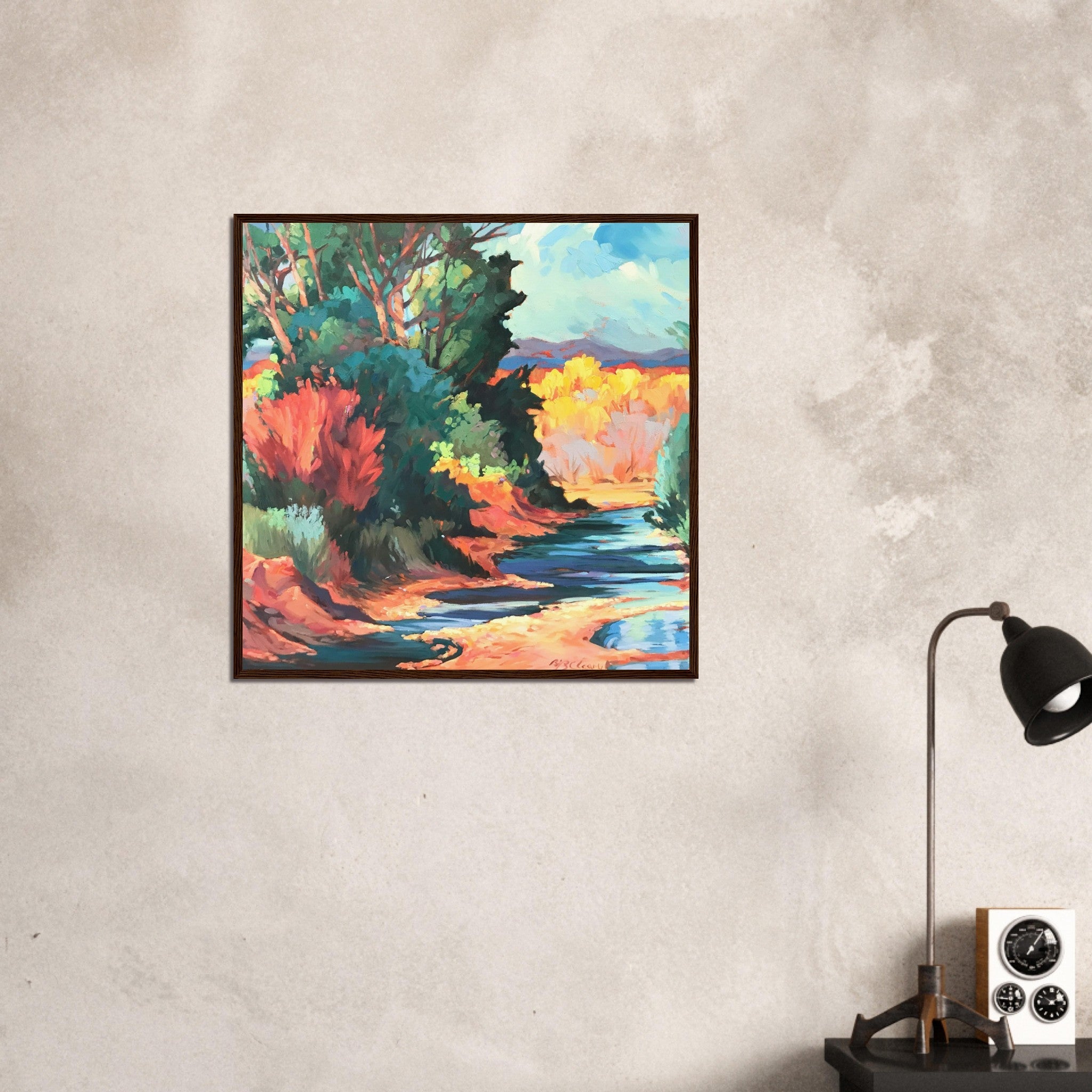 Framed painting of a colorful landscape on a textured wall with a lamp and clock below.