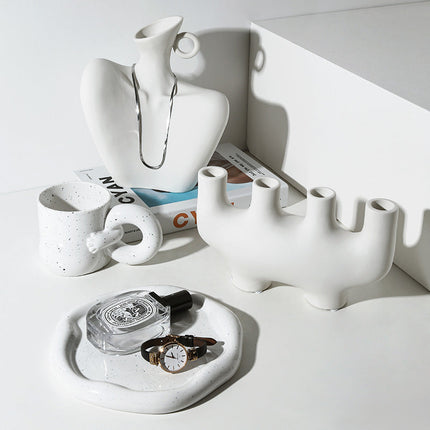 White ceramic items including a mug, vase, and decorative piece on a white surface.