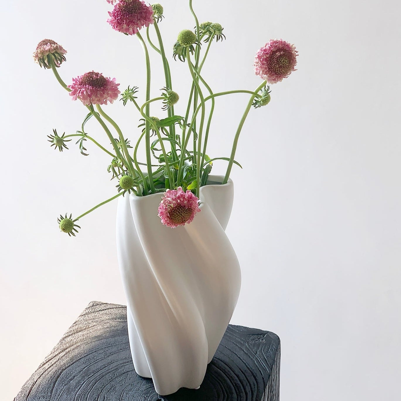 White wavy vase with pink flowers on a textured surface against a light background