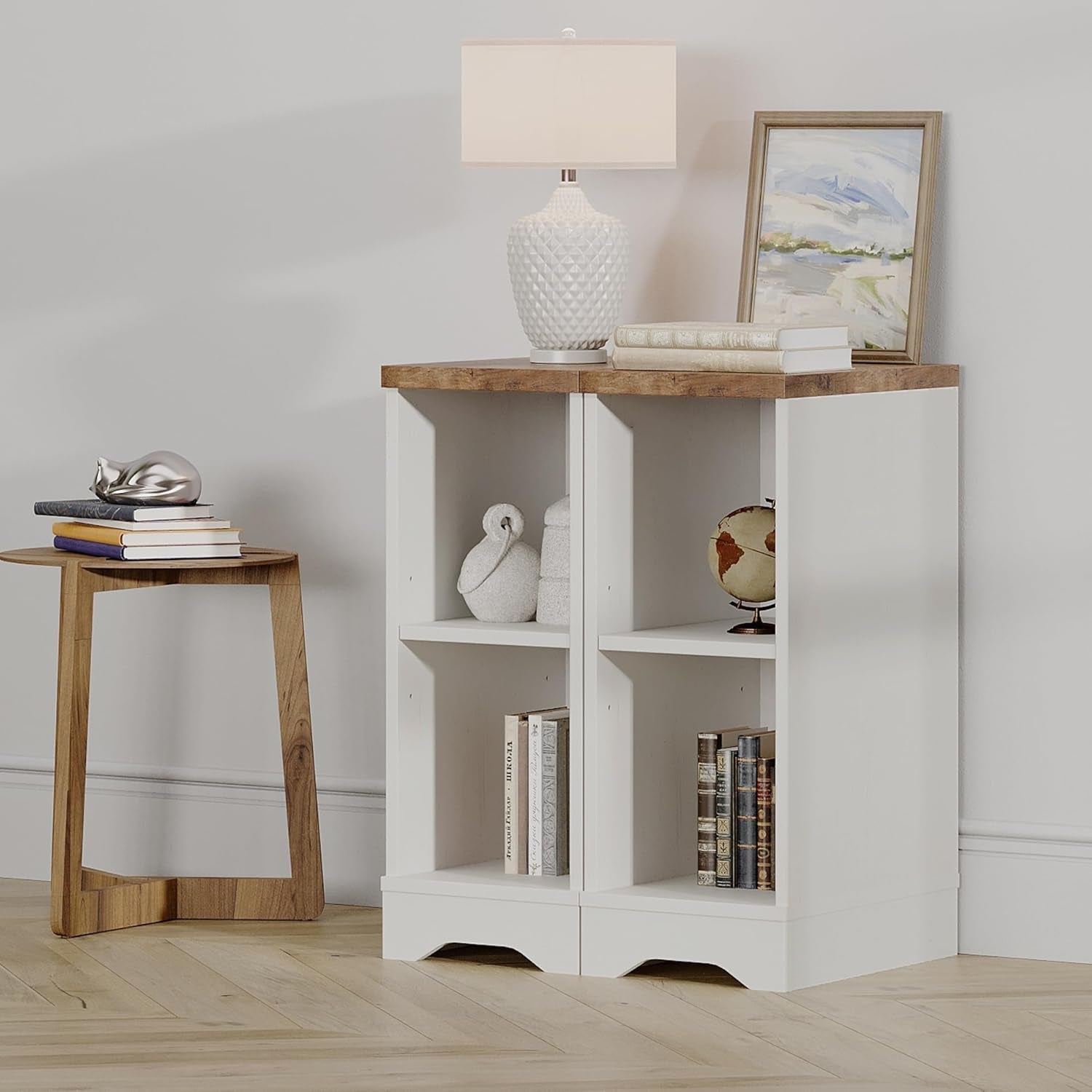 White bookshelf with wooden top against a light gray wall, with a small table and lamp in the foreground.