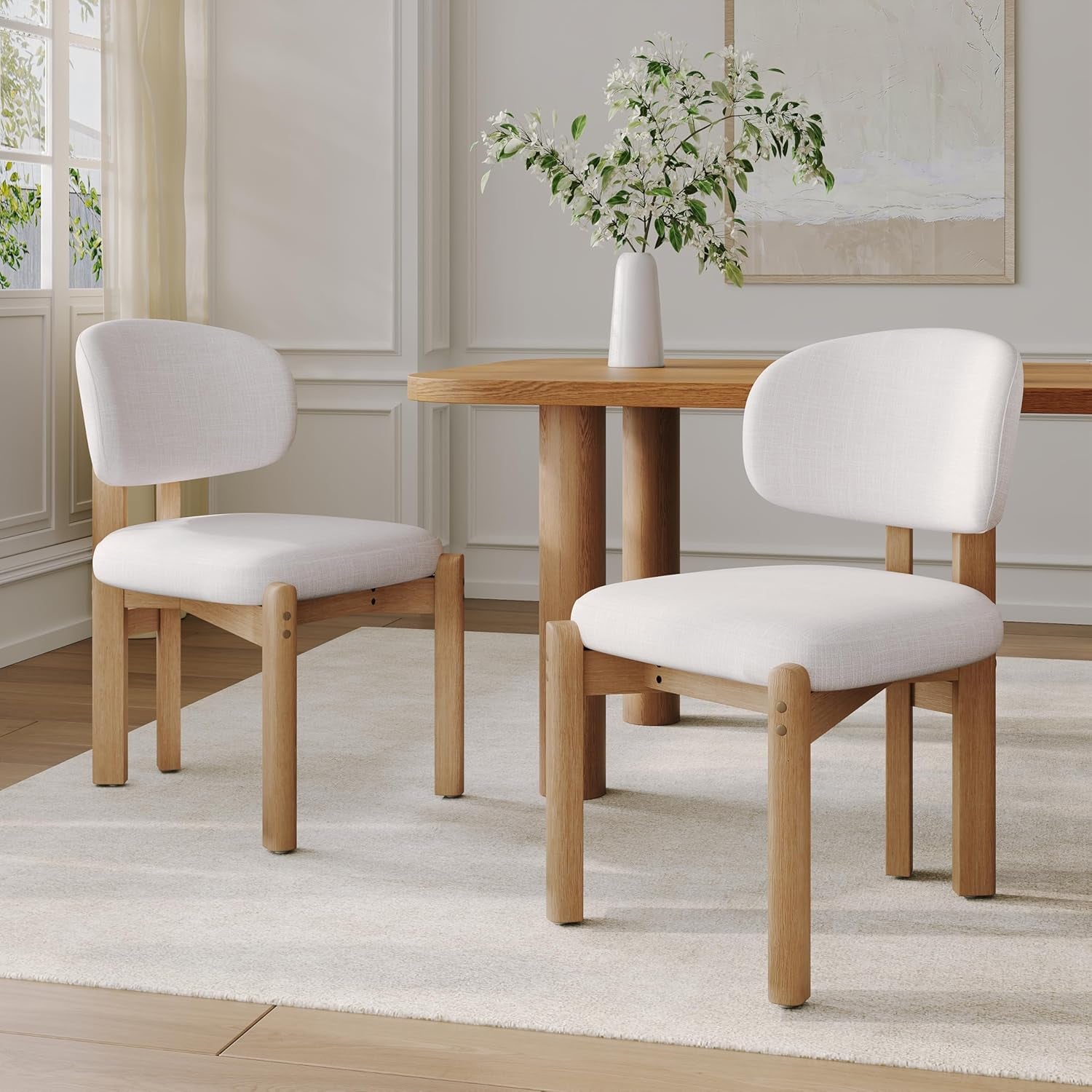 Two wooden chairs with white cushioned seats in a room with a table and decor.