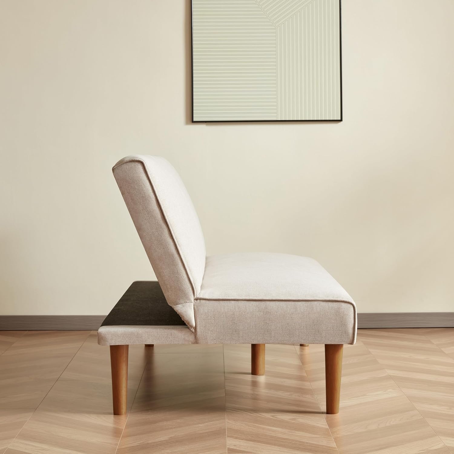 Beige chair with wooden legs on a wooden floor in a room with a framed picture on the wall.