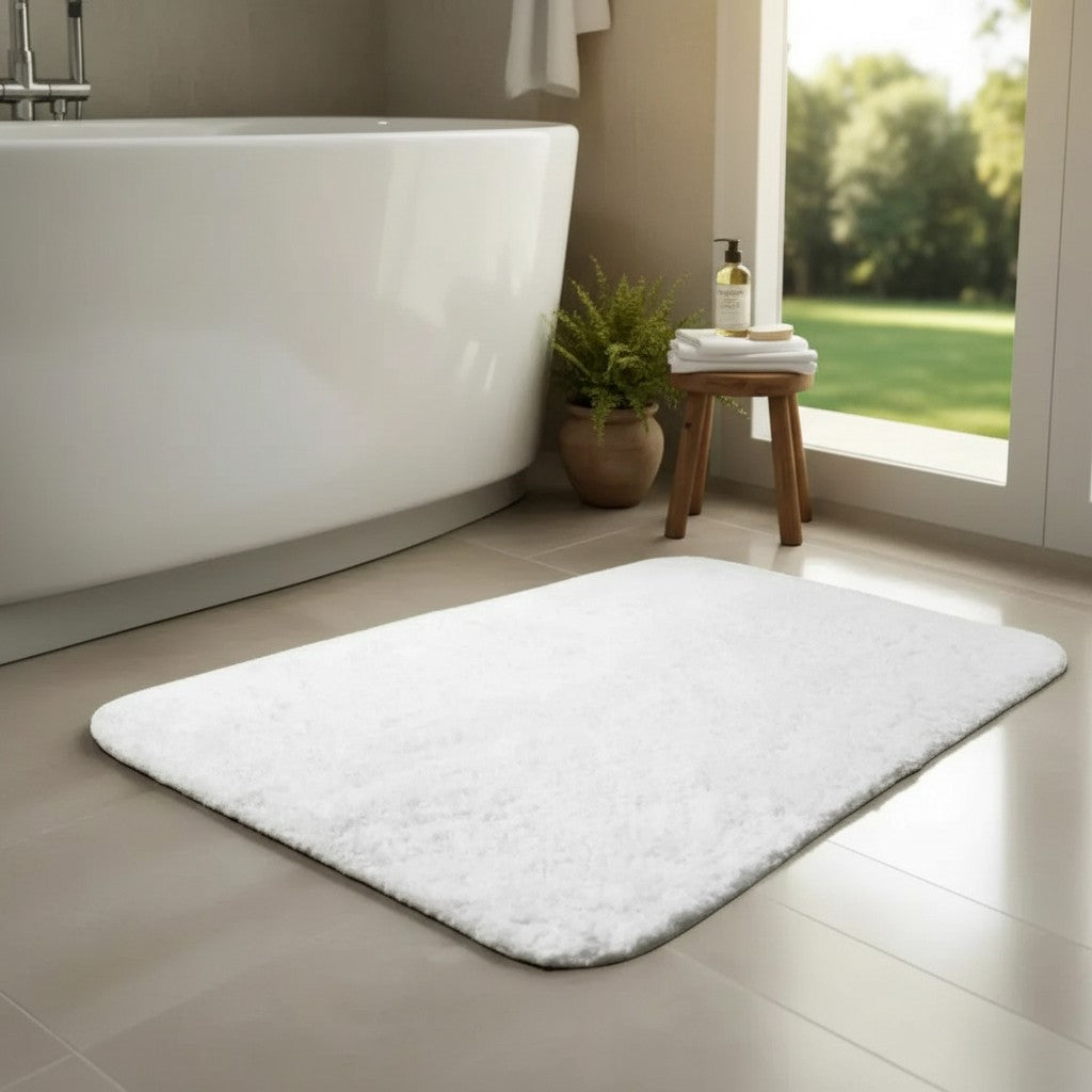White bath mat on a bathroom floor with a bathtub and window in the background