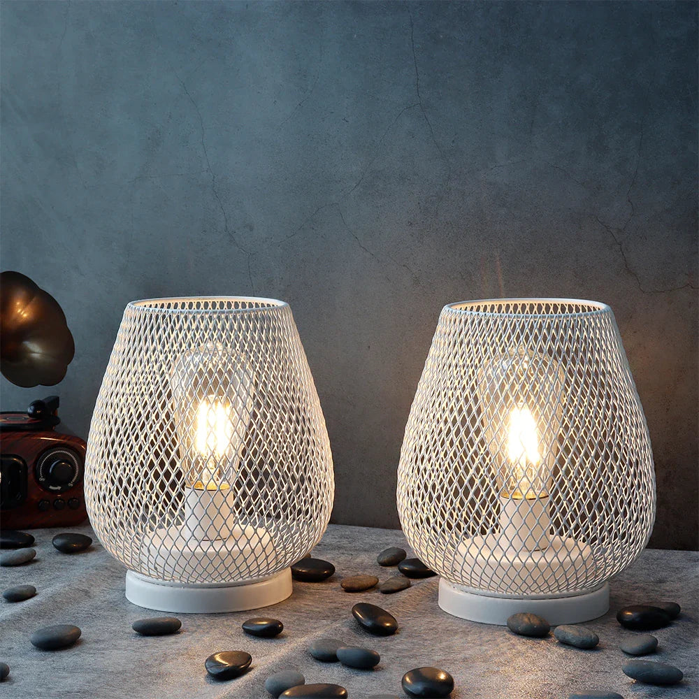 Two mesh-patterned lamps with glowing bulbs on a textured surface with stones.