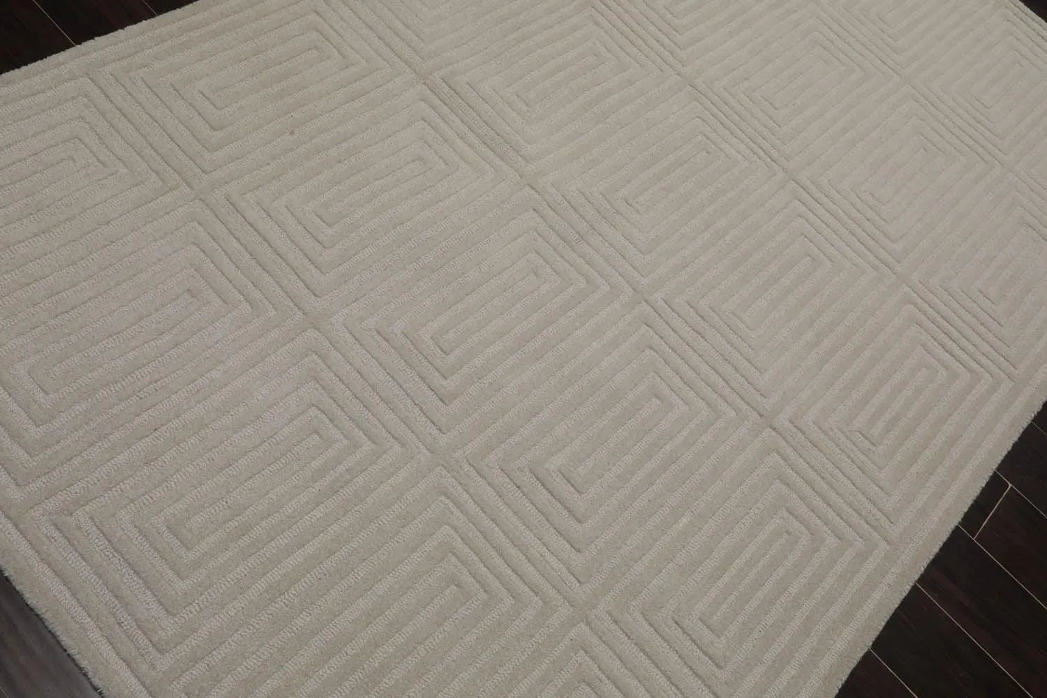 Textured beige rug with geometric pattern on a dark floor.