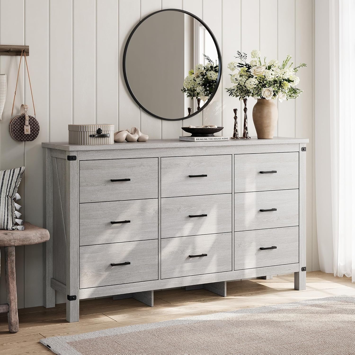 Gray dresser with round mirror and decorative items in a room with wooden floor and white walls.
