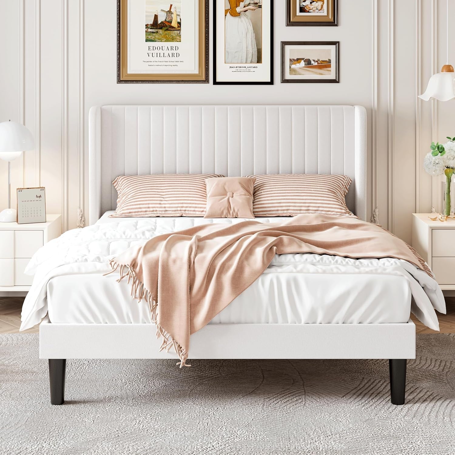 White upholstered bed with pink blanket and pillows in a bedroom setting.