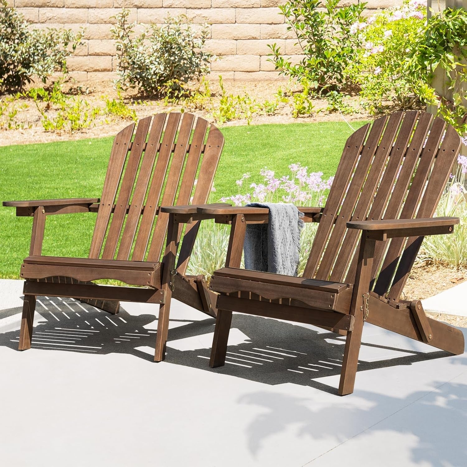 Two wooden Adirondack chairs on a patio with a garden background