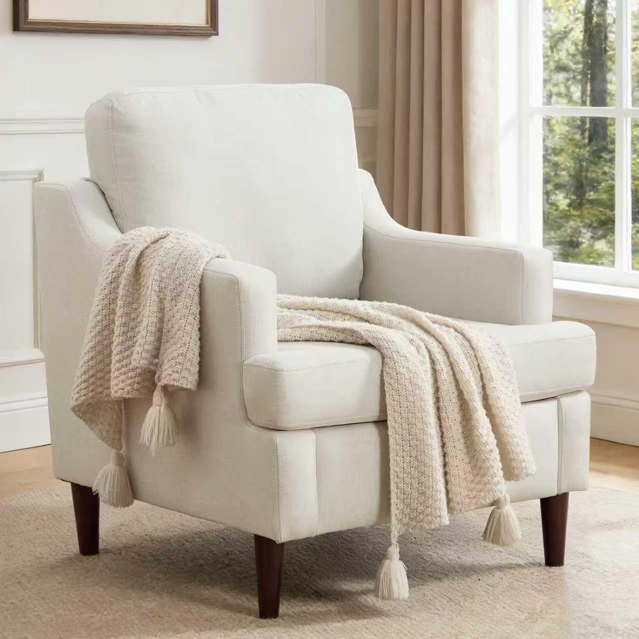 White armchair with a beige blanket draped over it in a room with a window and curtains.