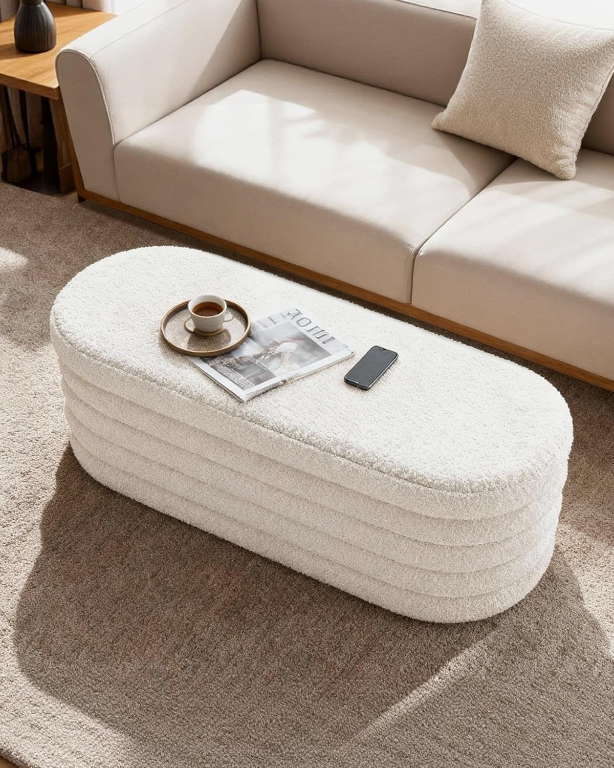 White ottoman with a cup, phone, and newspaper on top in a living room setting.