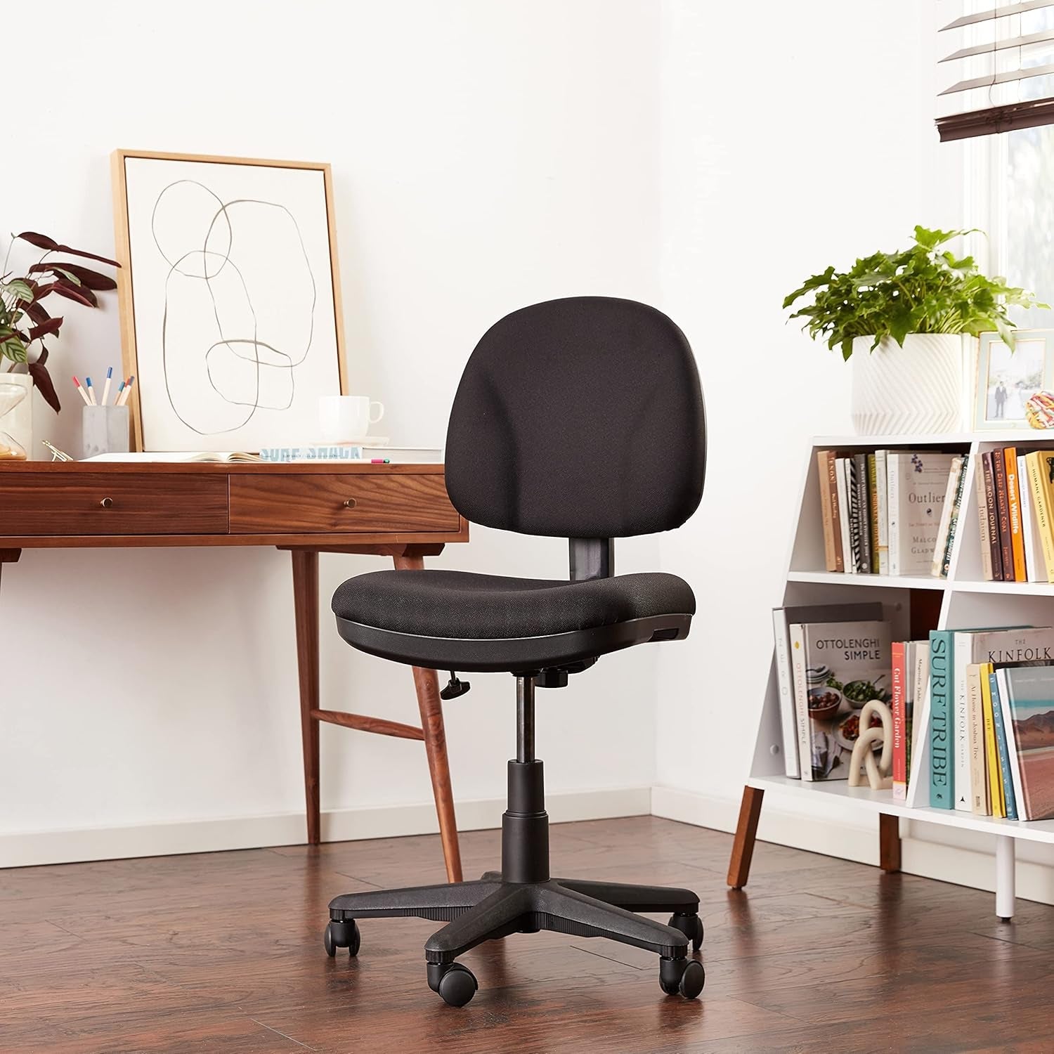 Black office chair in a home office setting with a desk and bookshelf.