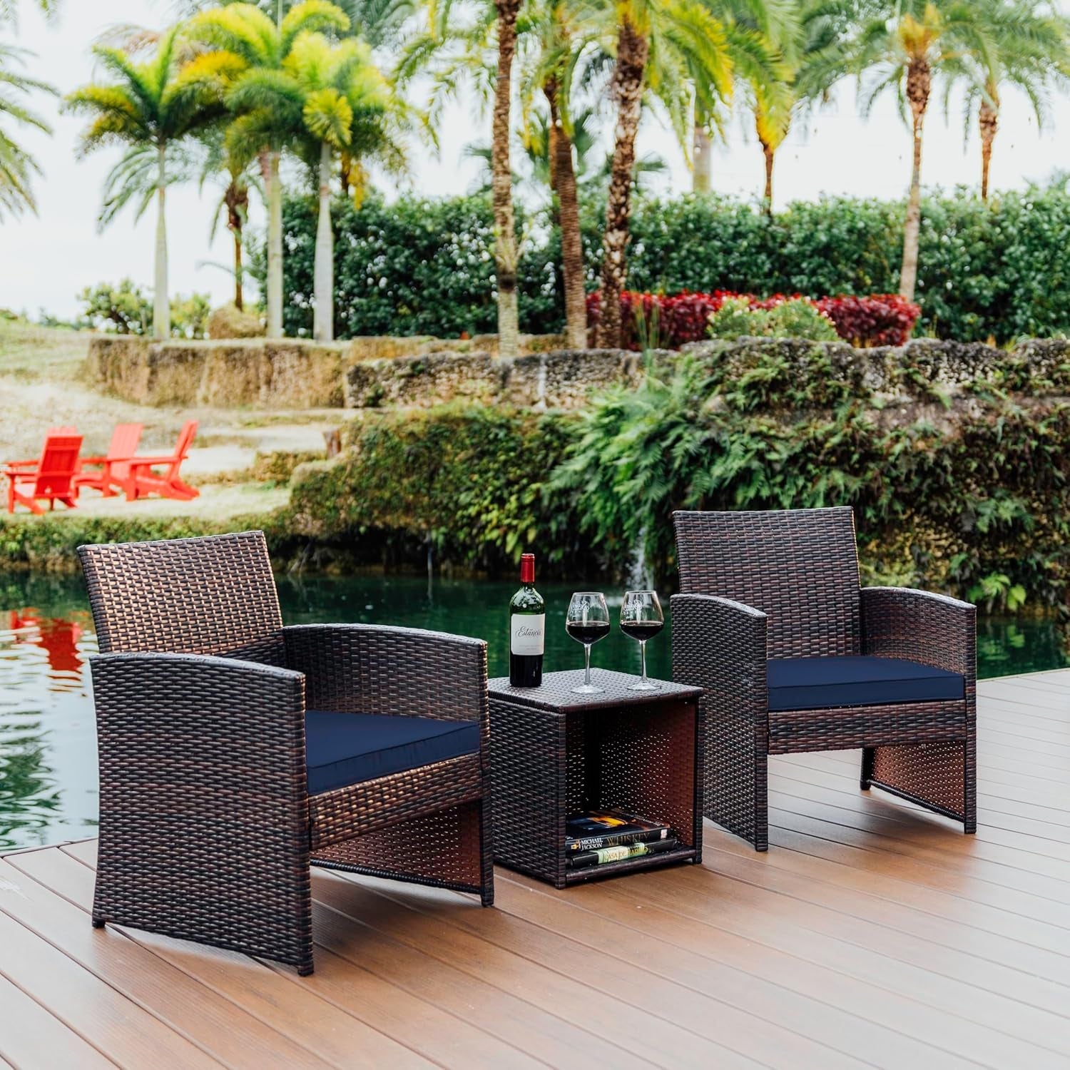 Two wicker chairs with cushions and a small table by a poolside with palm trees in the background.