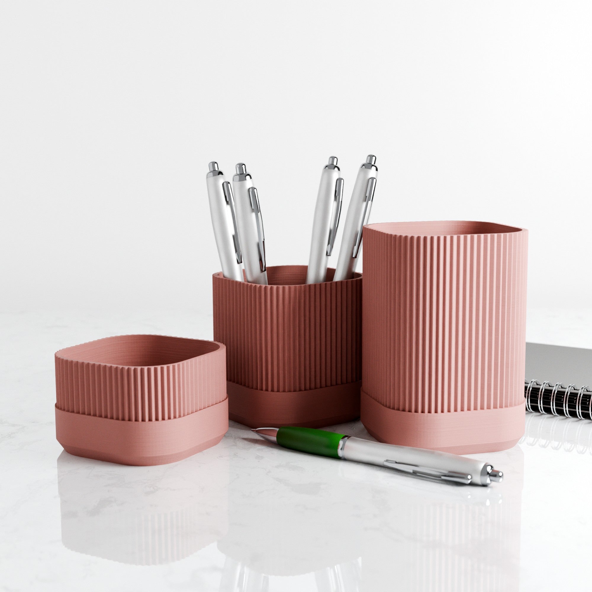 Set of pink and brown textured desk organizers with pens on a white surface.