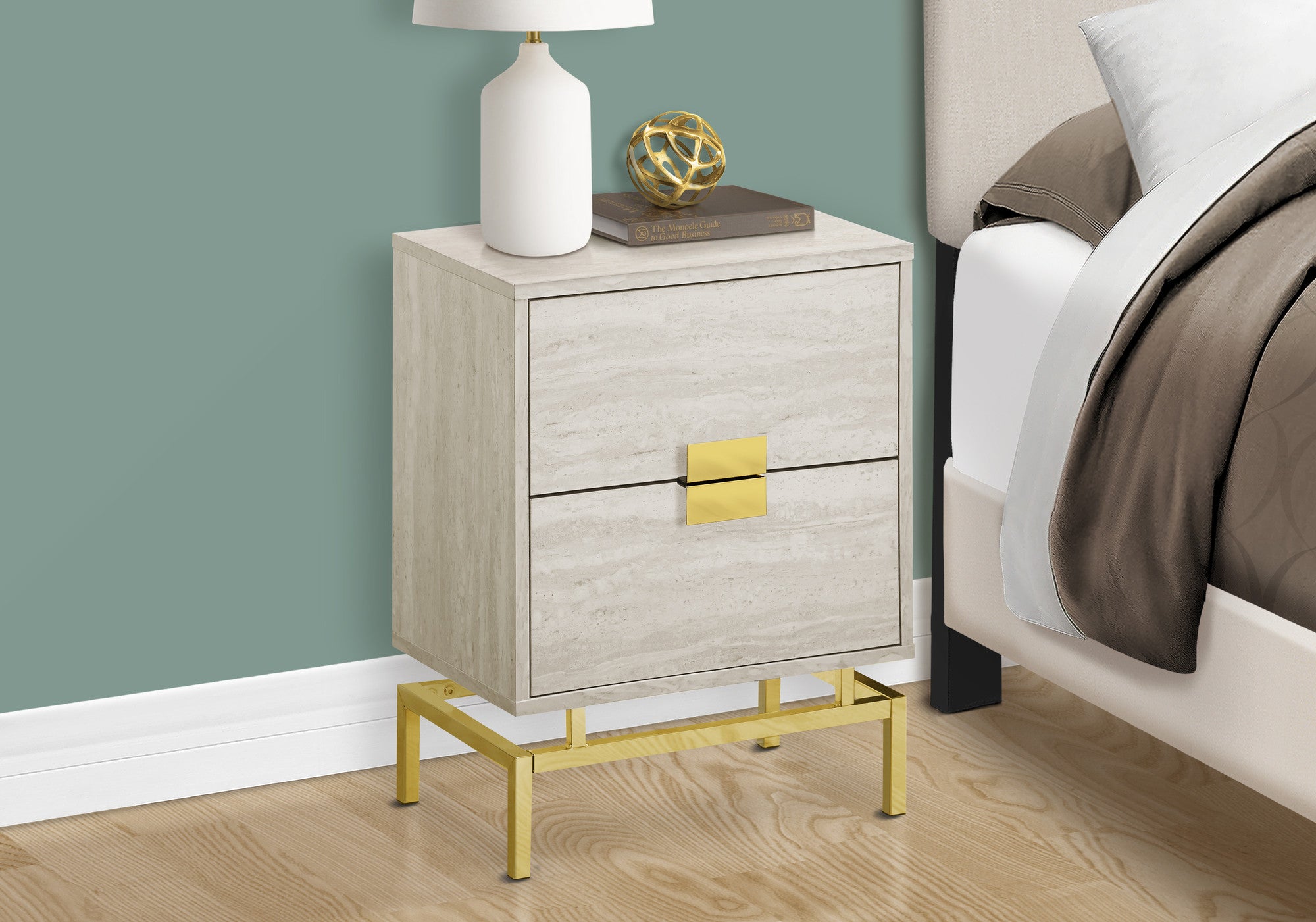 Beige nightstand with gold accents next to a bed with white and gray bedding.