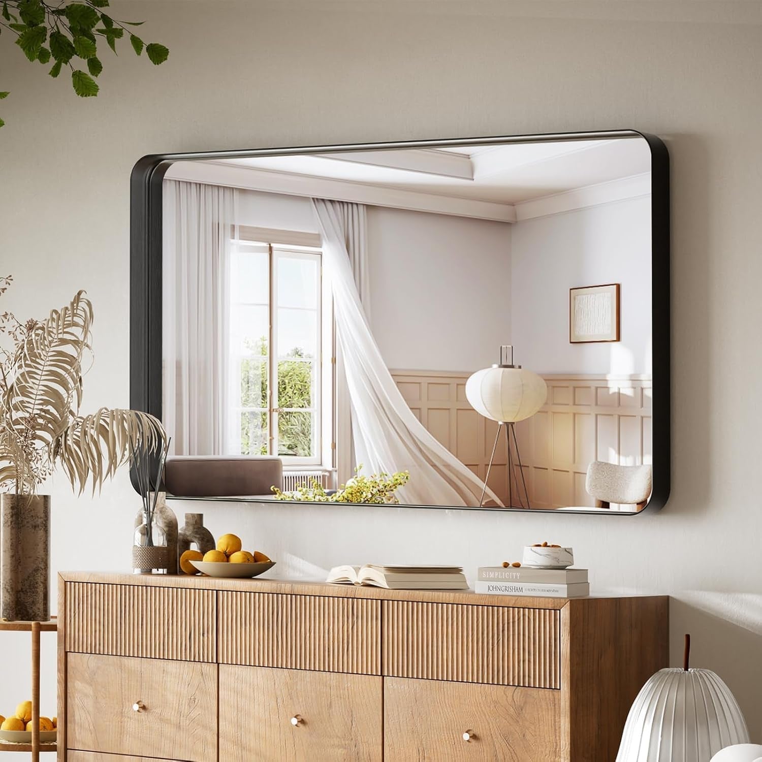 Large mirror on a wall above a wooden cabinet with decorative items.