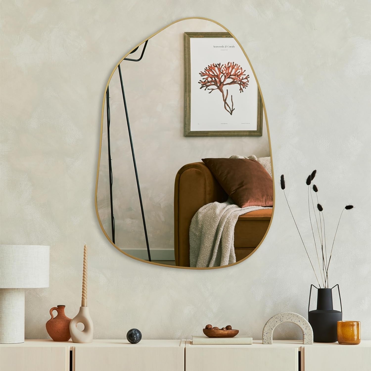 Round mirror on a wall with a framed artwork above, reflecting a cozy living room.