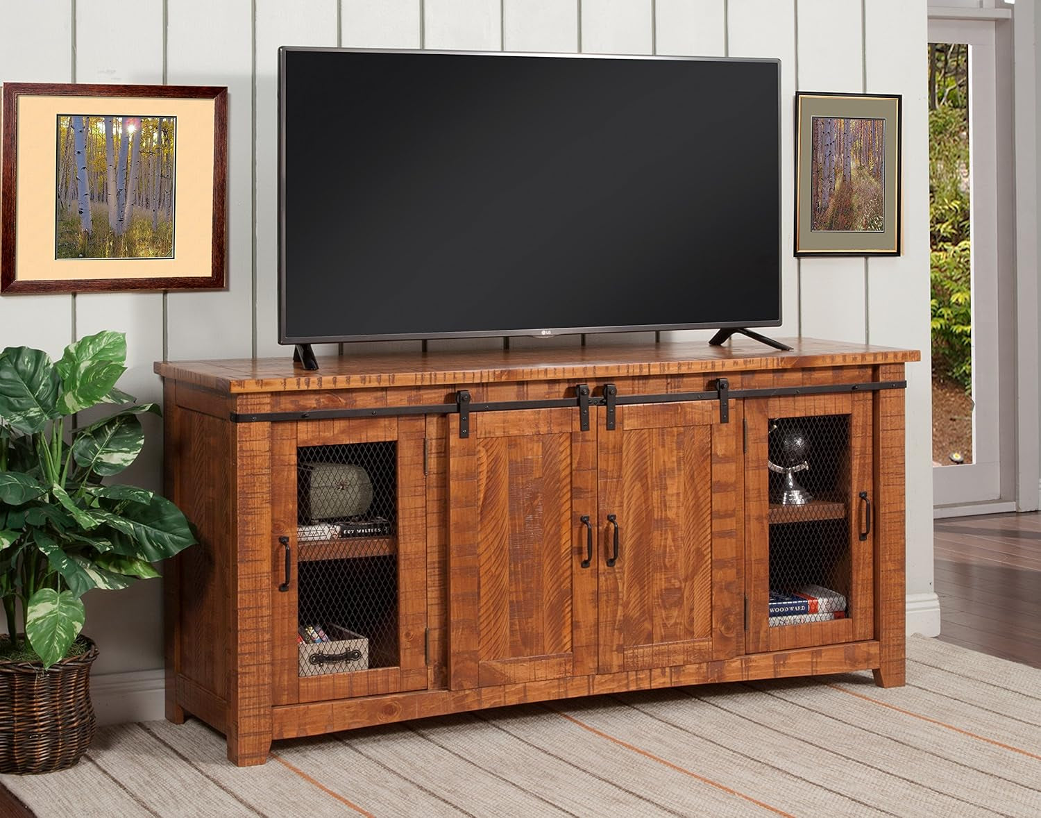 Wooden TV stand with a television on top in a room with plants and framed pictures.