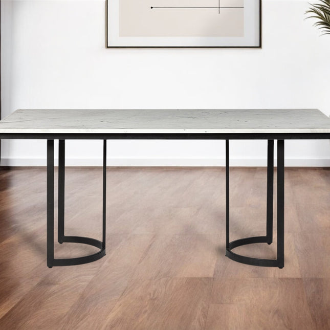 Modern dining table with marble-like top and black metal legs in a room with wooden flooring and a plant.