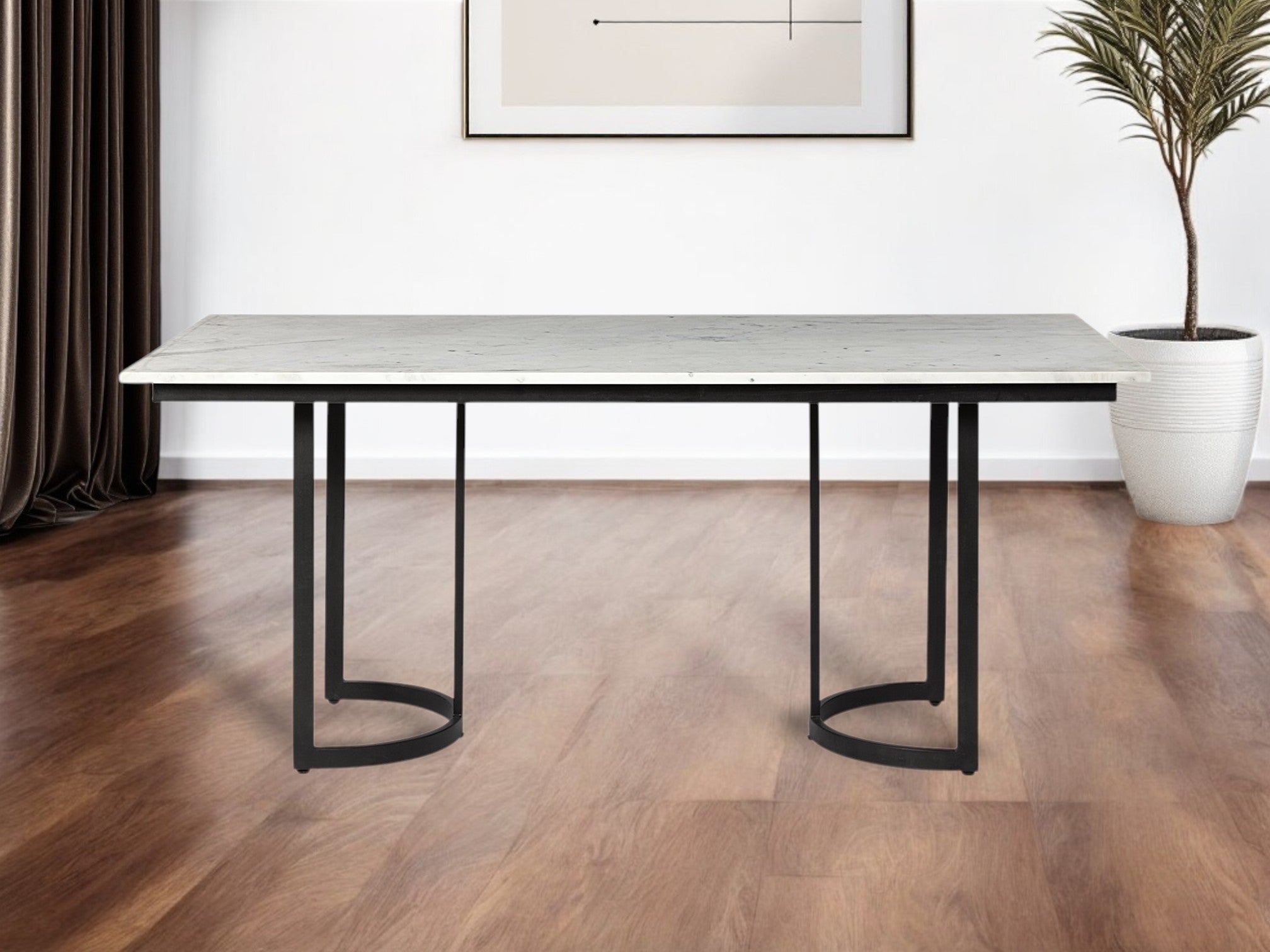 Modern dining table with marble-like top and black metal legs in a room with wooden flooring and a plant.