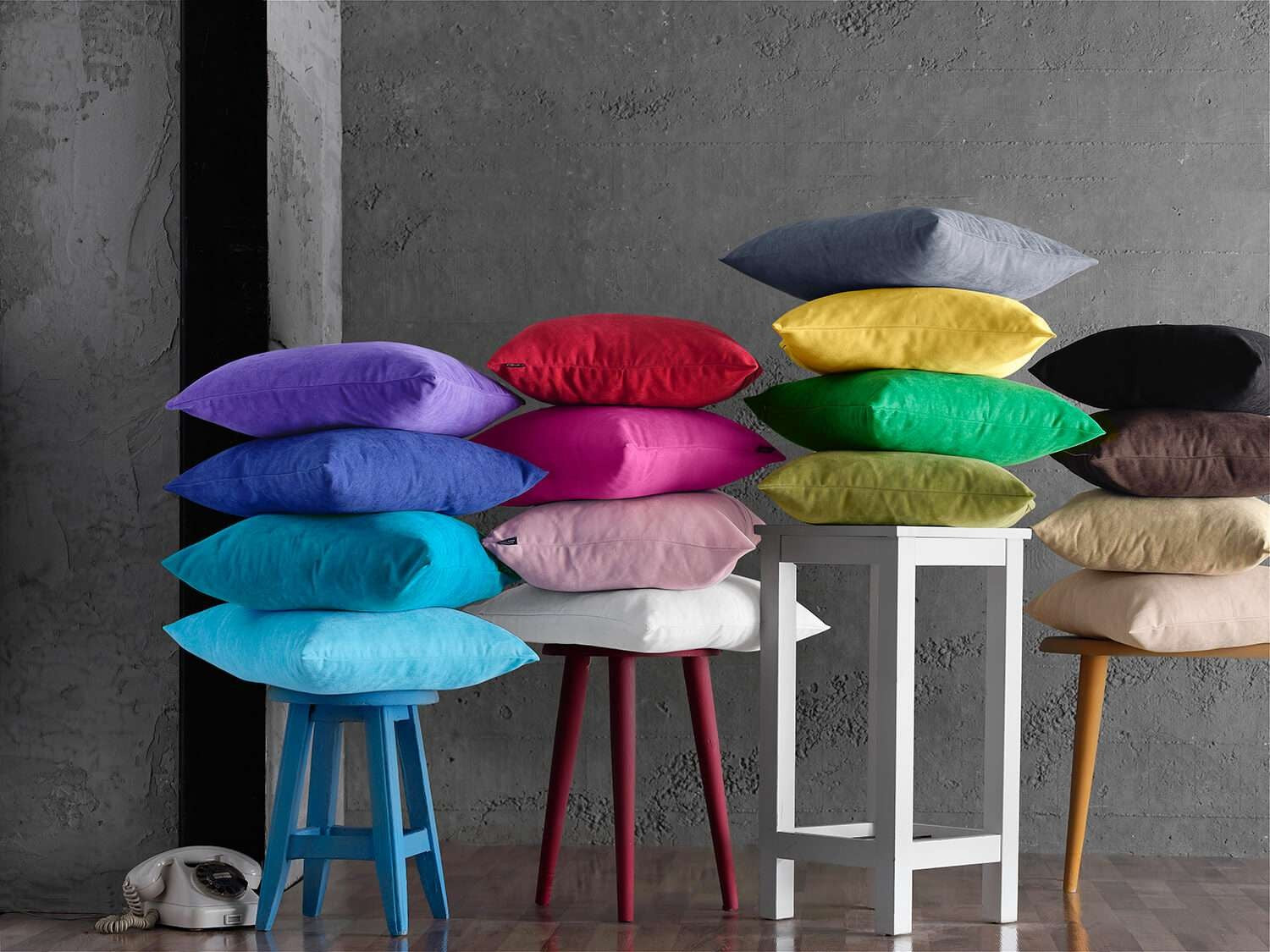 Colorful pillows arranged on stools against a gray wall.