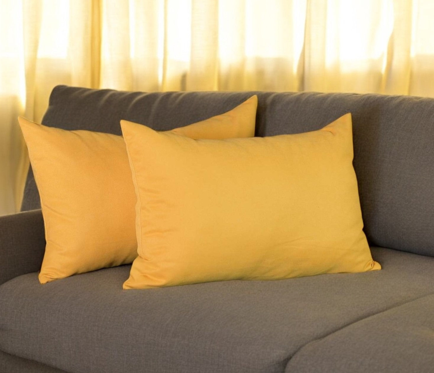 Yellow pillows on a gray sofa with light curtains in the background